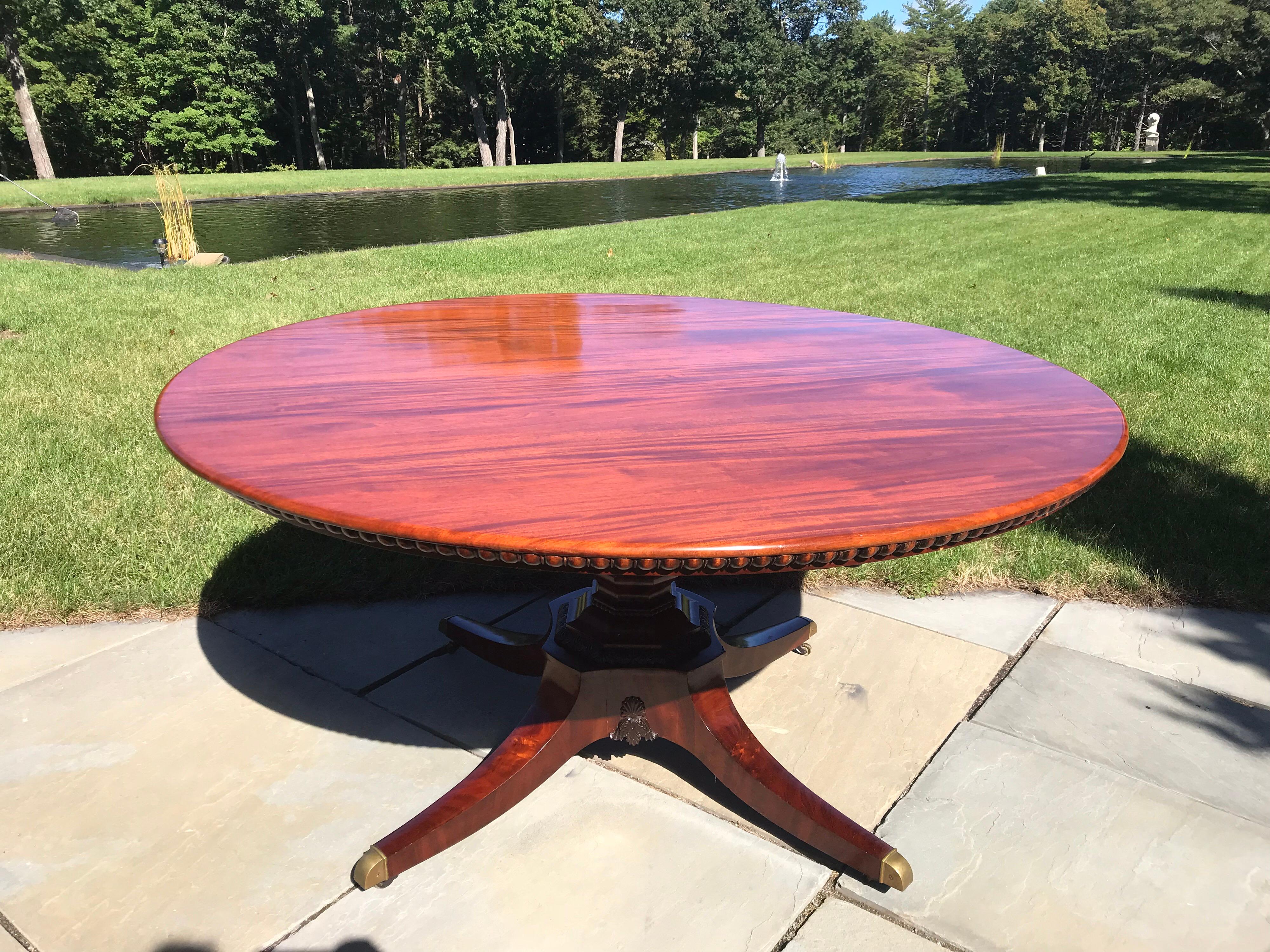 A most exquisite English Regency period mahogany 5’ diameter dining table or center table. The four legged pedestal has its original brass castor feet. The central shaft has finely carved neoclassical motifs. The solid mahogany top has a French