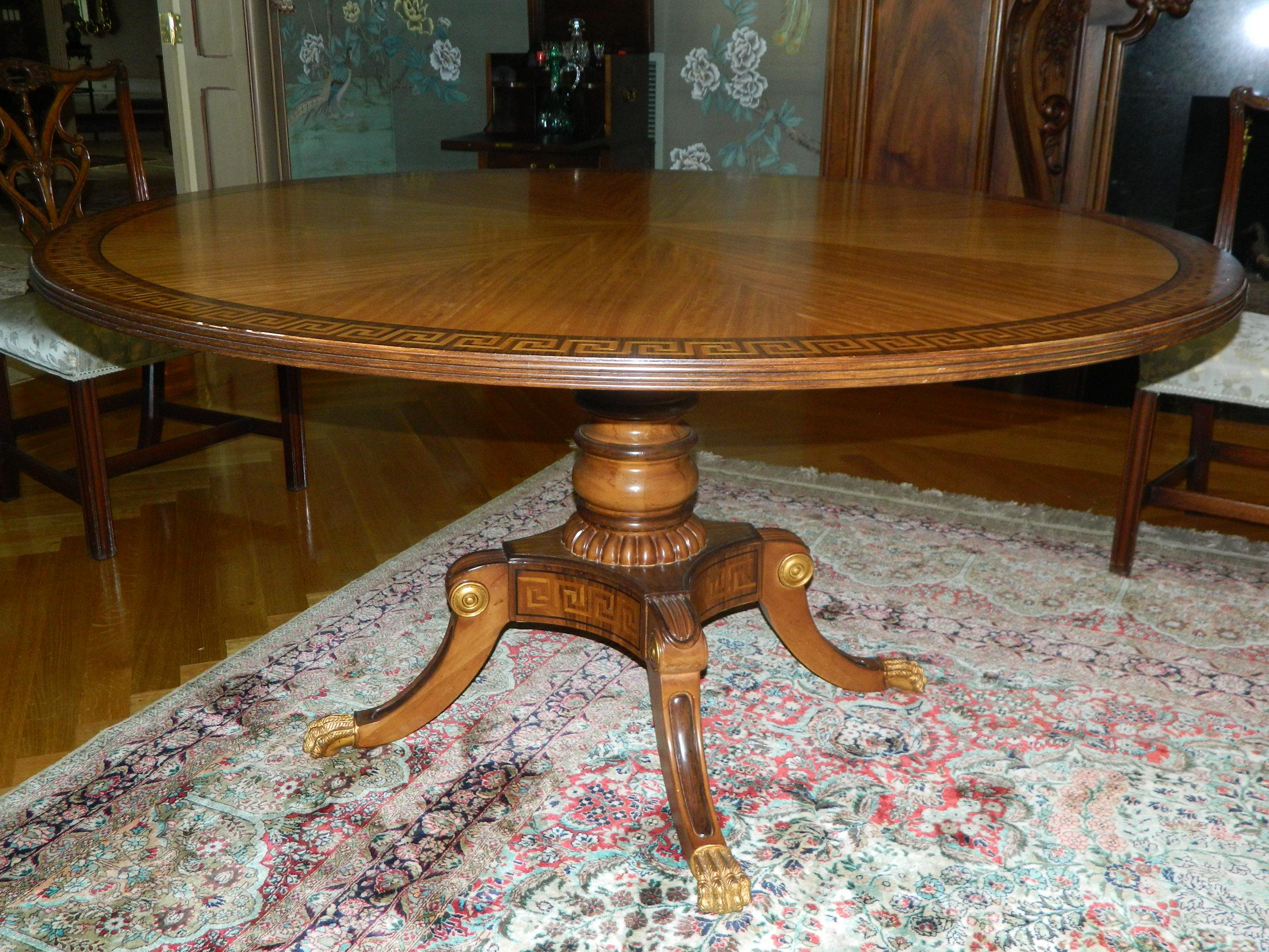 20th century mahogany round table with Greek key inlay on a decorative pedestal and gold painted paw feet.
  