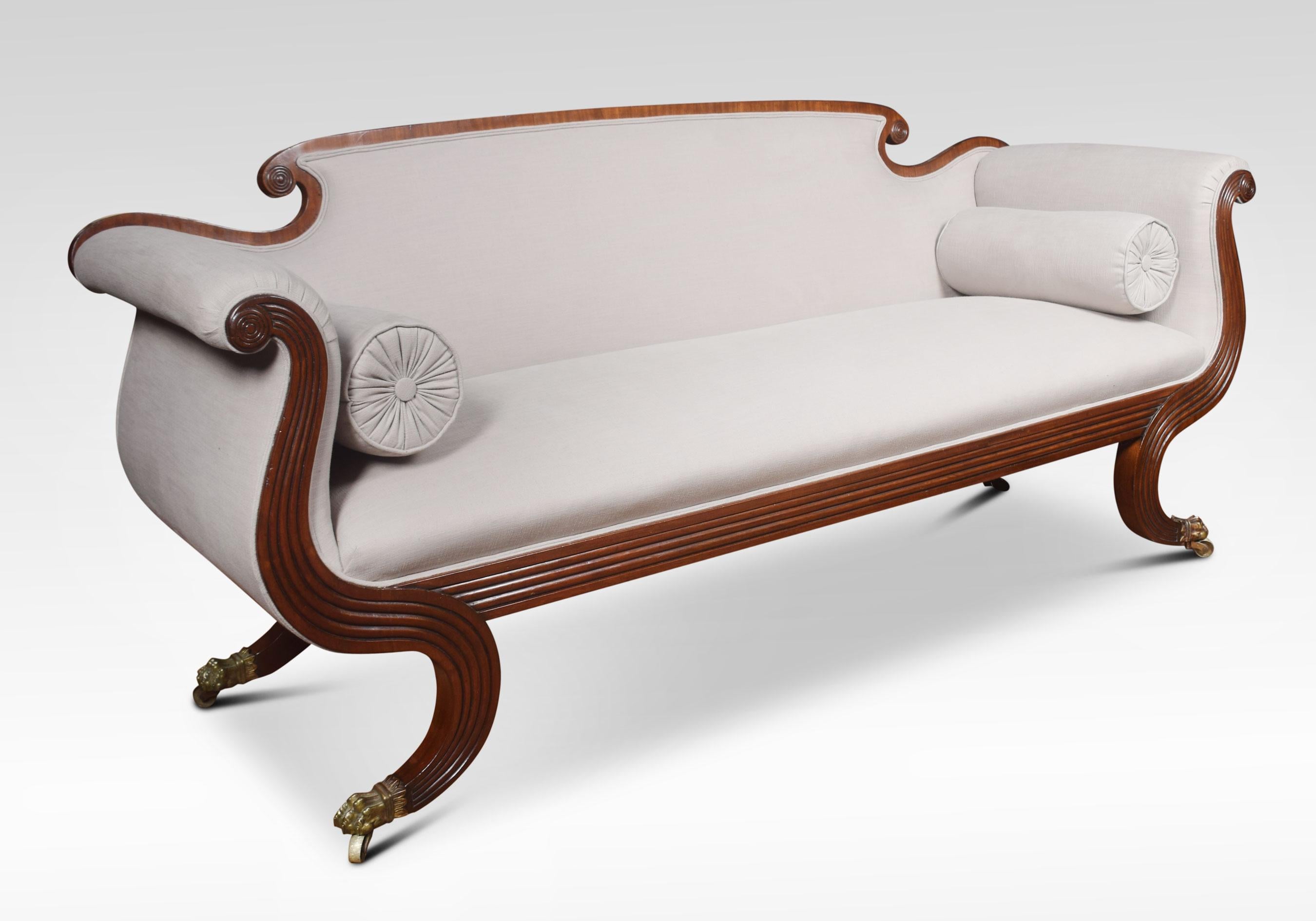 A mahogany show frame scroll end sofa, having shaped back with carved roundels and reeded decoration. To the recently upholstery back seat and scroll arms with loose bolster cushions. All raised up on sabre legs with brass paw feet and