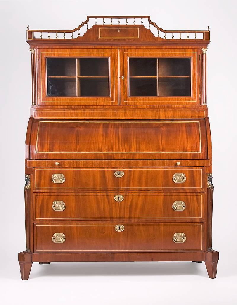 A secretaire with a display case top manufactured in the Empire style in the late 19th century. The mahogany is veneered on oak creating a mirrored veneer picture. A three-parted substructure with brass fittings and flanking caryatid pilasters. By