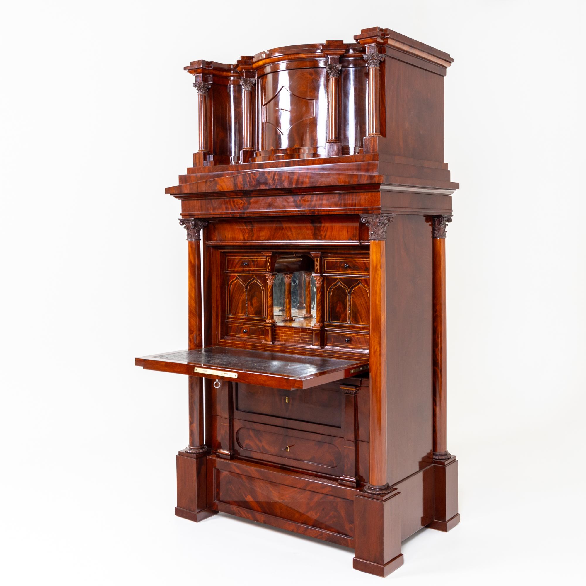 Large Berlin top secretaire from the 1830s made of solid and veneered mahogany. The secretaire rests on a high plinth with a drawer and faceted front. Above it rise two lateral full columns with bases, smooth shafts and Corinthian capitals. The