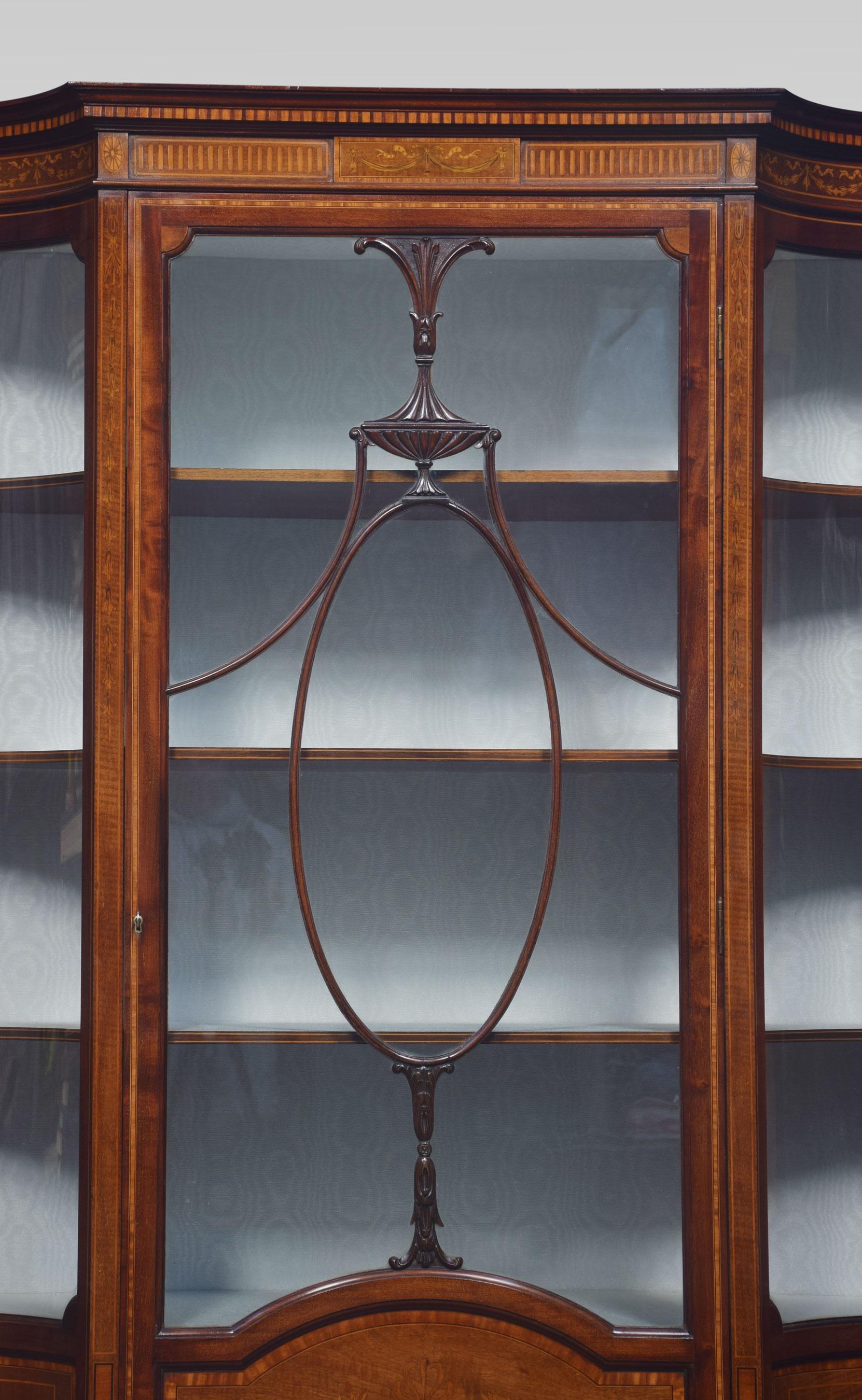 Late 19th Century mahogany Sheraton revival inlaid display cabinet the moulded top above inlaid freeze. To the central door with acanthus ribbons and vase motif opening to reveal upholstered shelved interior. Flanked by concave glazed panels above