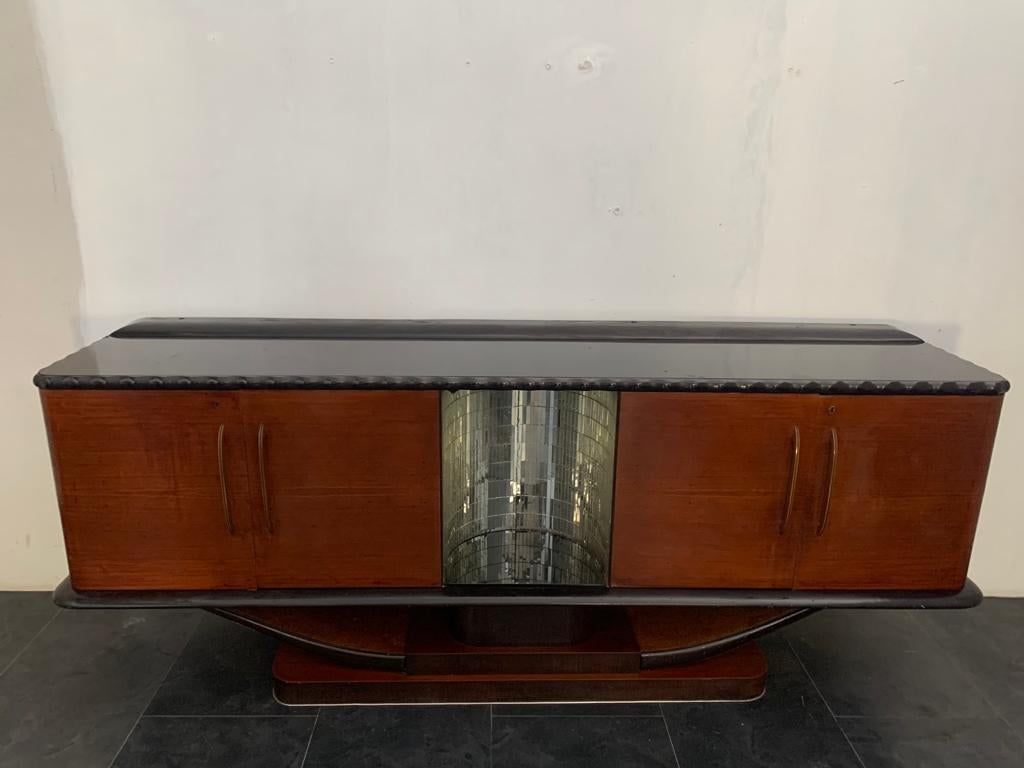 Sideboard in mahogany ebonized profiles, with niche in mosaic mirror for sculpture, black crystal top, brass handles.
Shelves are missing.