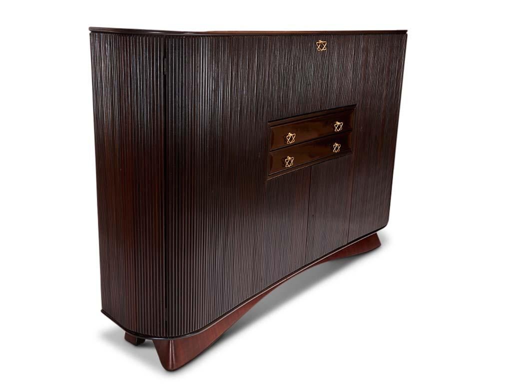 Mahogany Sideboard / Bar by Osvaldo Borsani

Cabinet features two large doors concealing six shelves, one drop-front dry bar with one glass shelf and bin, two drawers, and two lower doors concealing open storage with an additional drawer.
