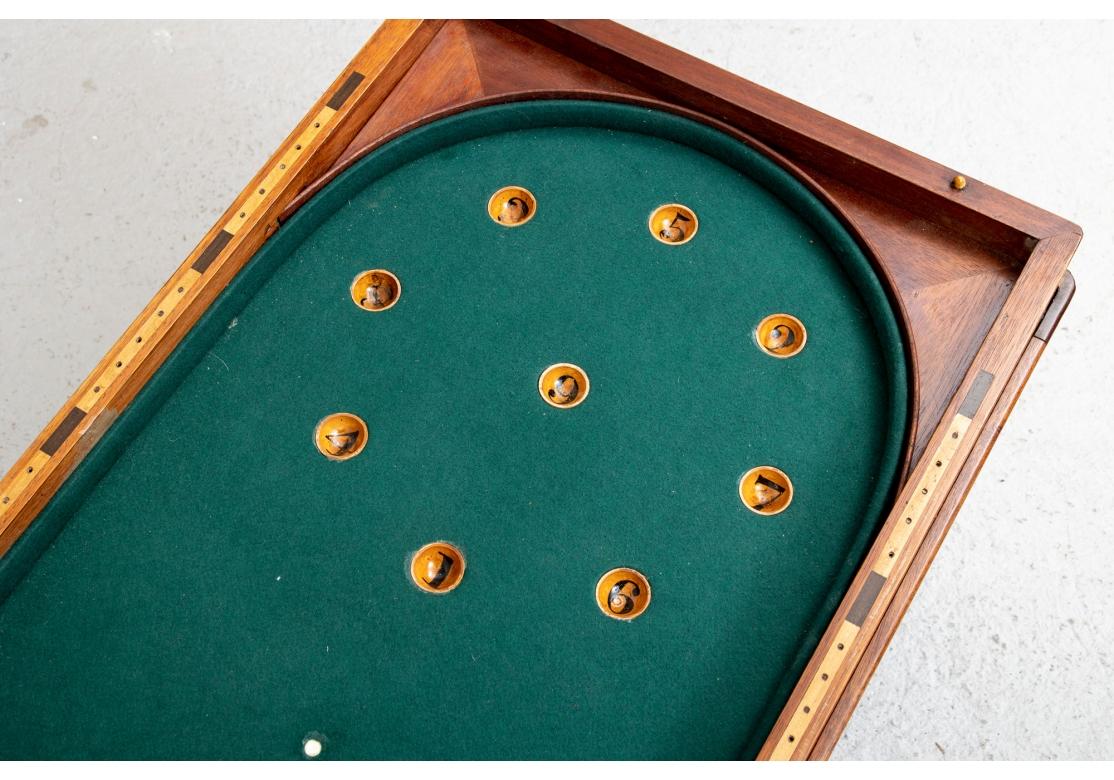 Mit aufklappbarem Deckel und Messinghaken und -ösen. Das Innere ist mit grünem Filz ausgekleidet und mit nummerierten Holzvertiefungen versehen. Fehlende Spielfiguren. Auf einem separaten Ständer mit geschnitzten Beinen. 

L. 36 1/2