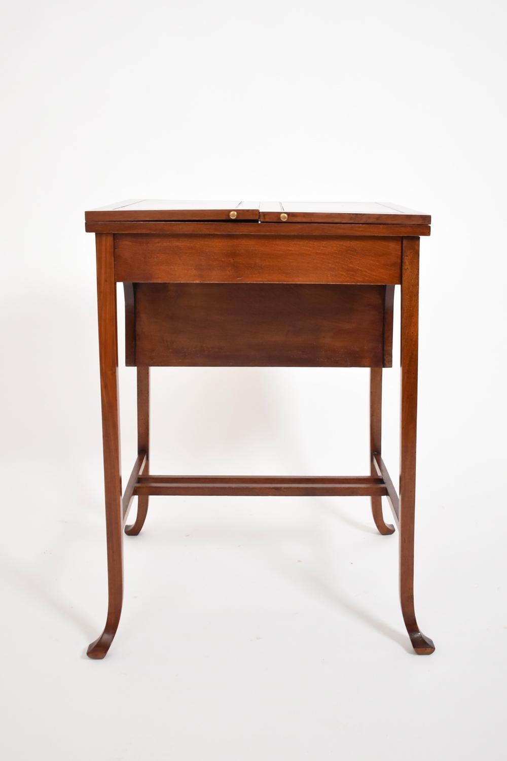 Mahogany desk table with top with two lift-up flaps, folding top with dividers for letters and drawers, writing surface in burgundy-toned leather, square-section legs. England, late 19th c.