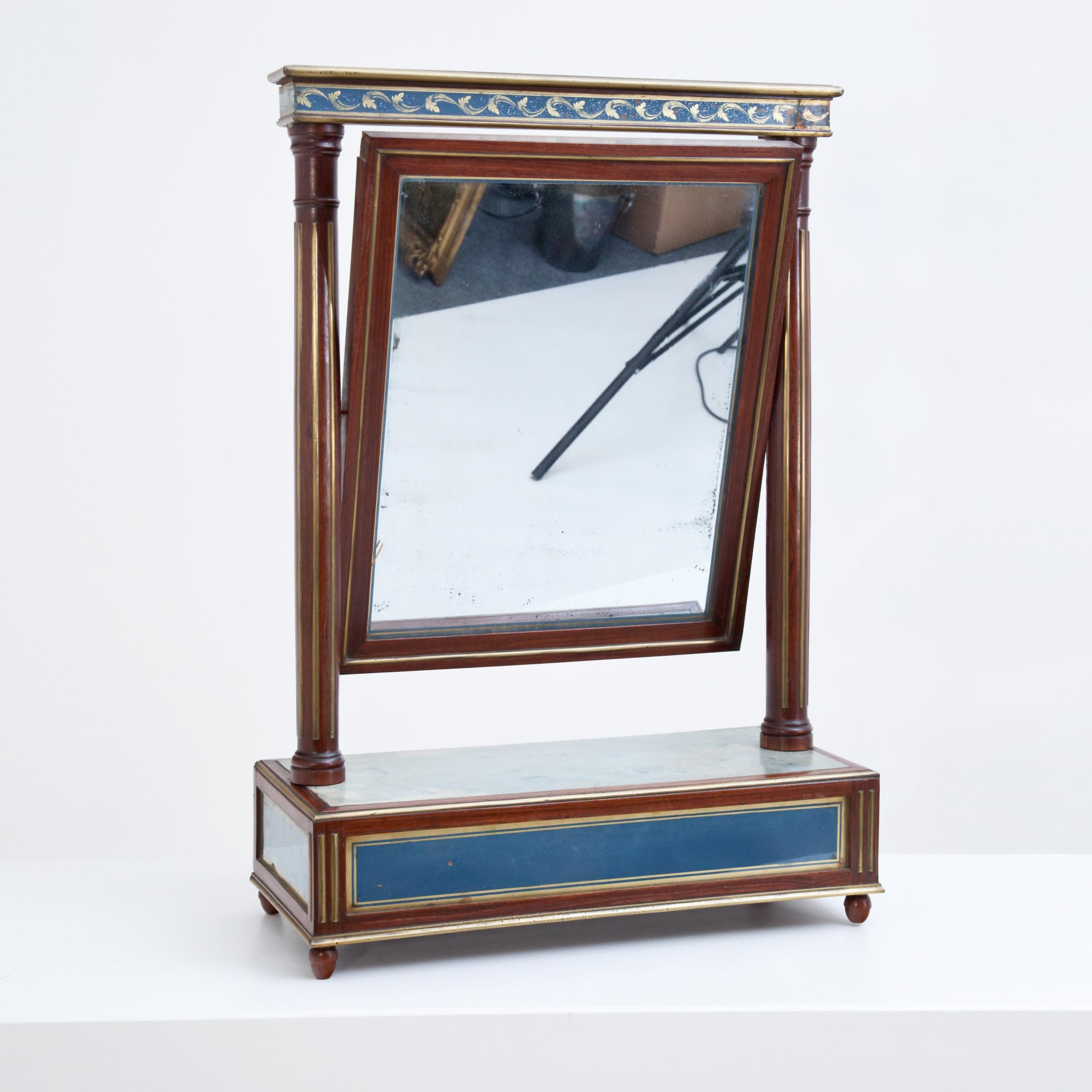 Klassizistischer Tischspiegel aus Mahagoni mit Intarsien aus Verre églomisé in Blau und Gold. Der Spiegel ist zwischen kannelierten Säulen mit geradem Architrav und Zapfen montiert.
