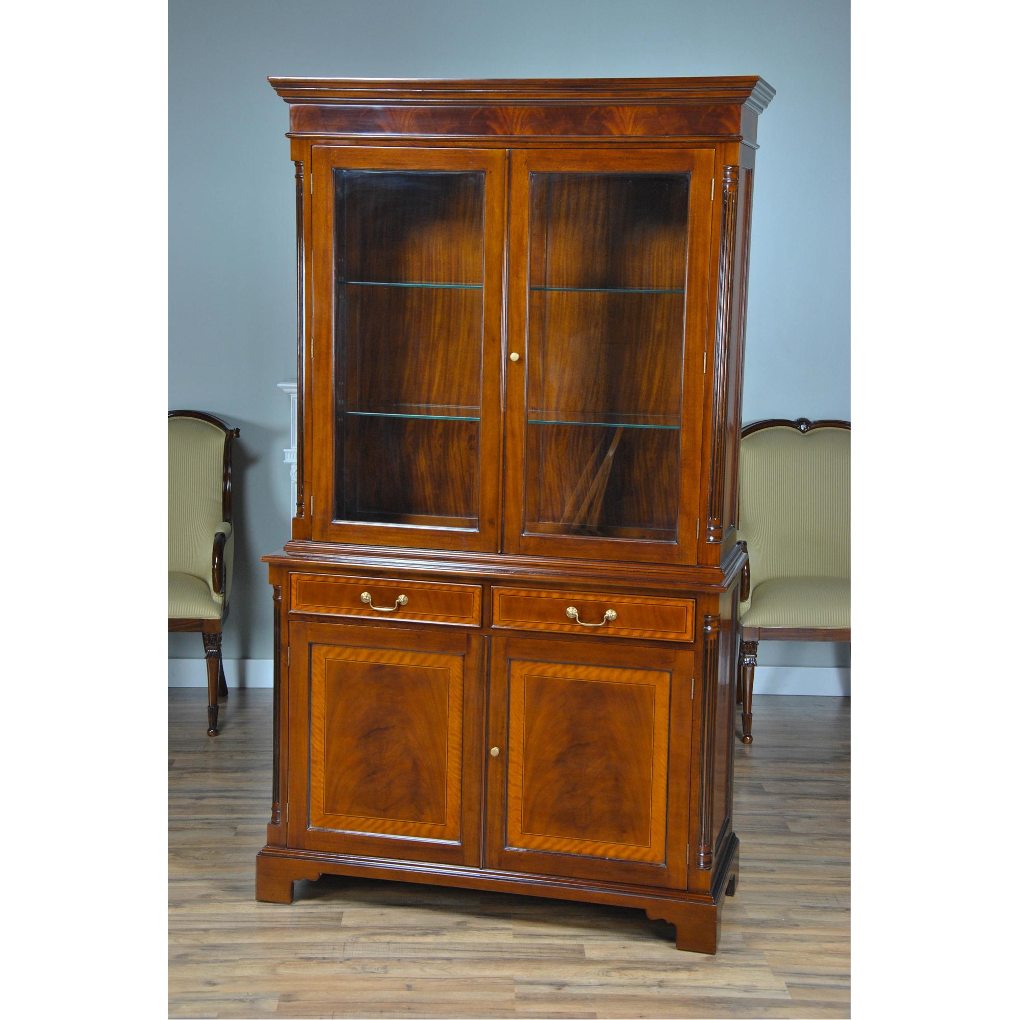 A highly functional and decorative two part Mahogany Tall Bookcase cabinet resting on shaped bracket feet. Large doors without lattice work allow for full presentation of your decorative items while glass shelves in the top section allow for light