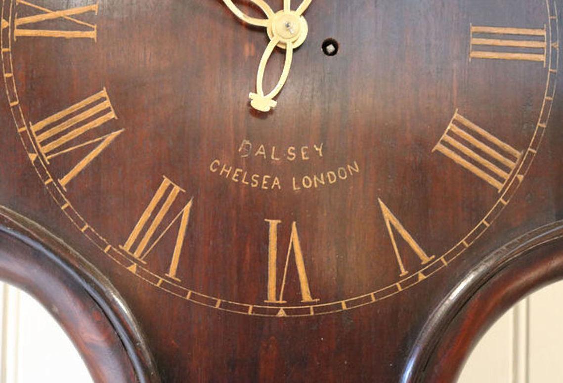 A solid mahogany English Tavern clock, made at the beginning of the 20th century, with a period fusee movement. The 18th century styled case has a shaped and pegged dial with gilt numeral and brass hands and is named Dalsey, Chelsea. It has an 8 day