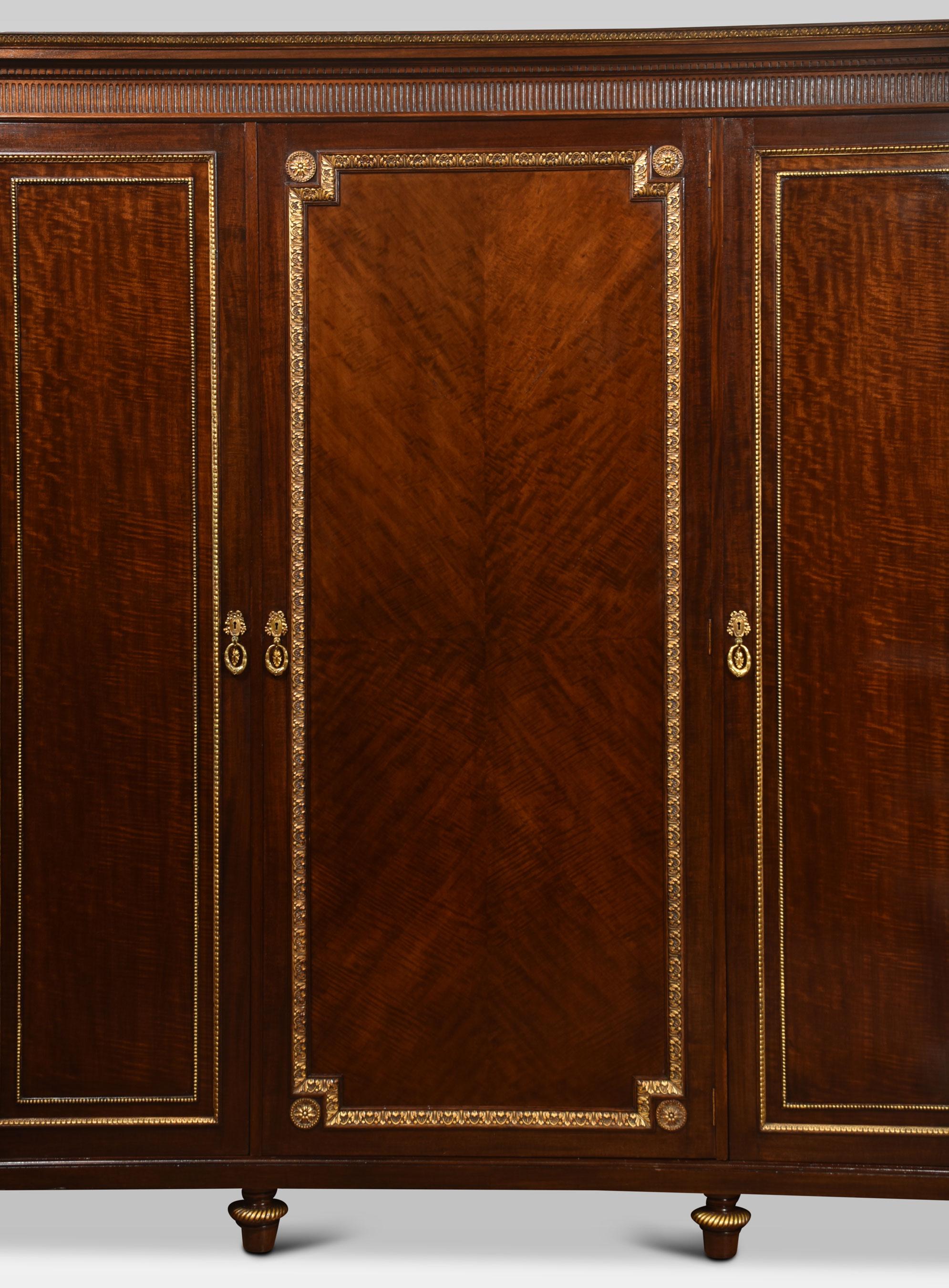 Mahogany wardrobe the carved moulded cornice above three long well figured mahogany doors with gilt-wood moulding. Opening to reveal a fitted interior with drawers, sliding trays and two large hanging areas. All raised up on turned