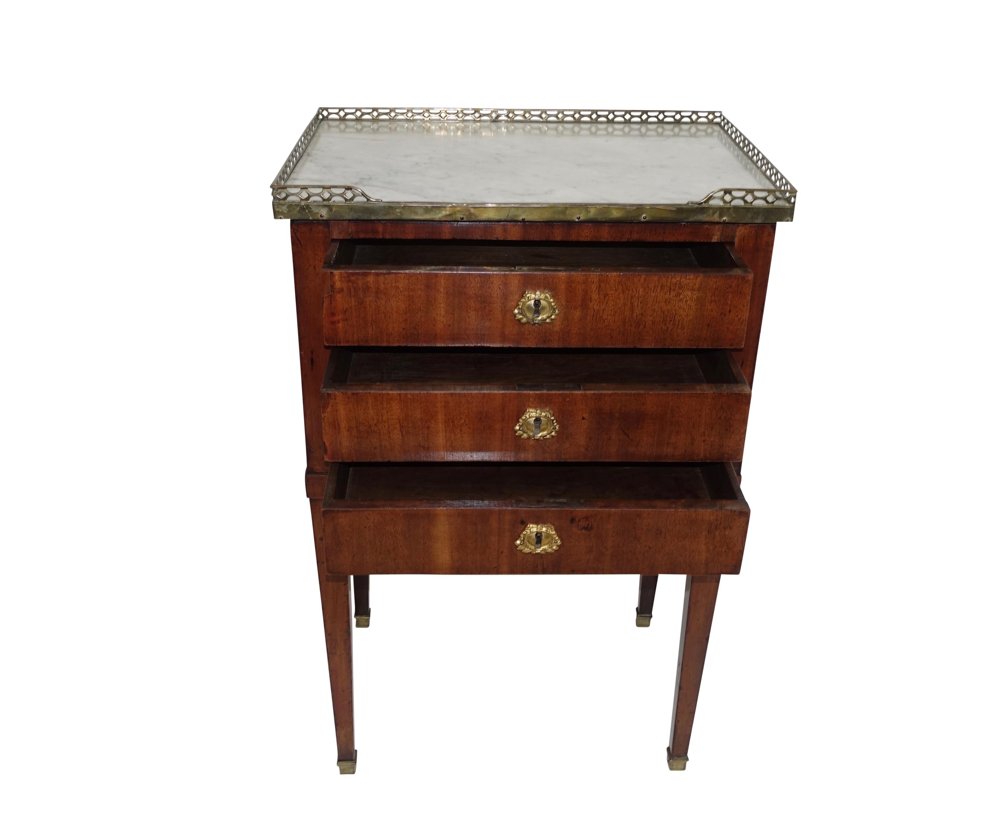 Louis XVI style mahogany work table with pierced brass gallery around the white marble top surface, having three drawers, and standing on square tapering legs ending in brass sabots. France circa 1830

