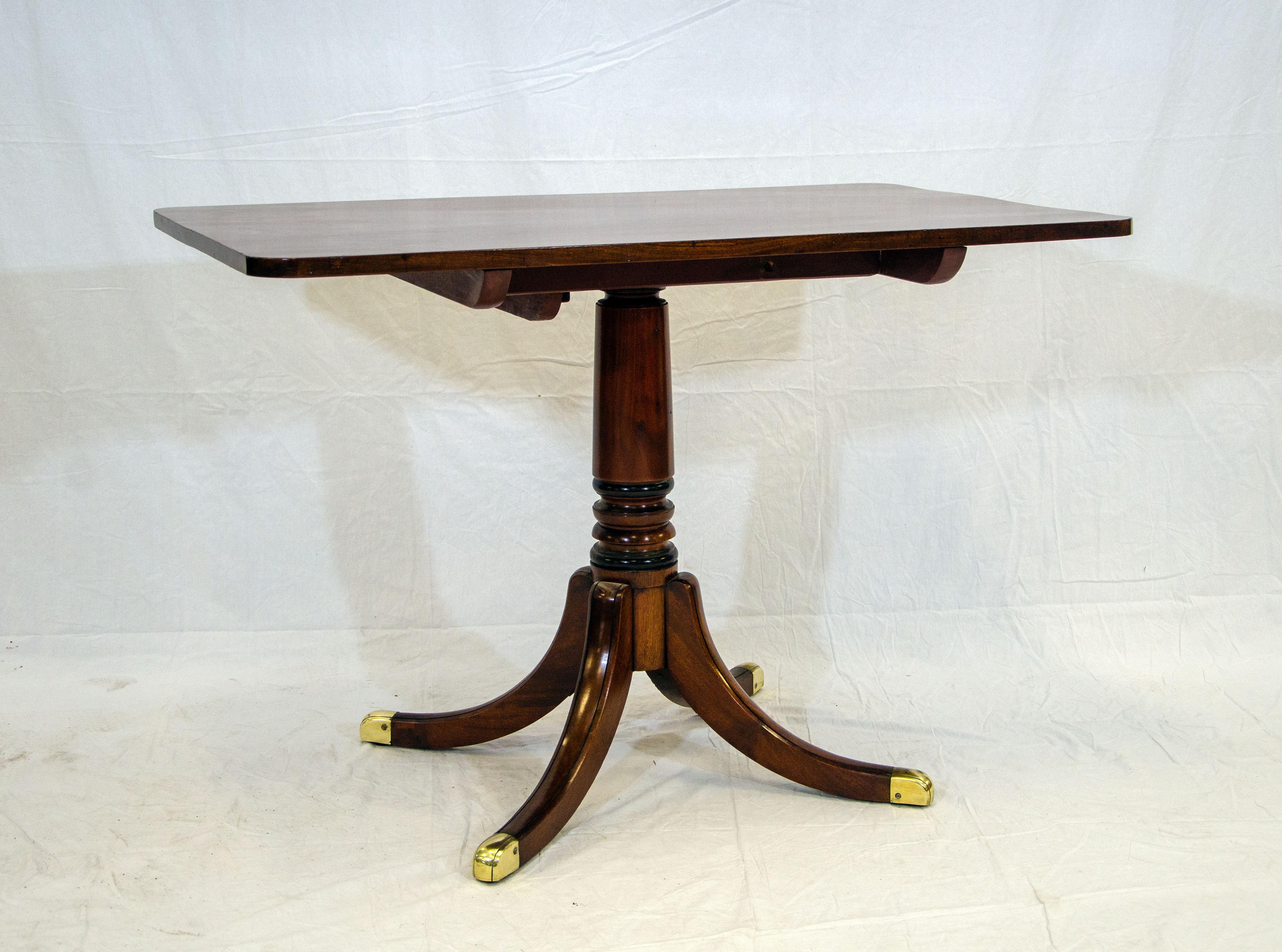 Duncan Phyfe style mahogany tilt-top table with a very nice original finish. The center pedestal has a turned section above the four legs with brass caps. There are latches on the underside to tilt the top for storage. The center pedestal has about