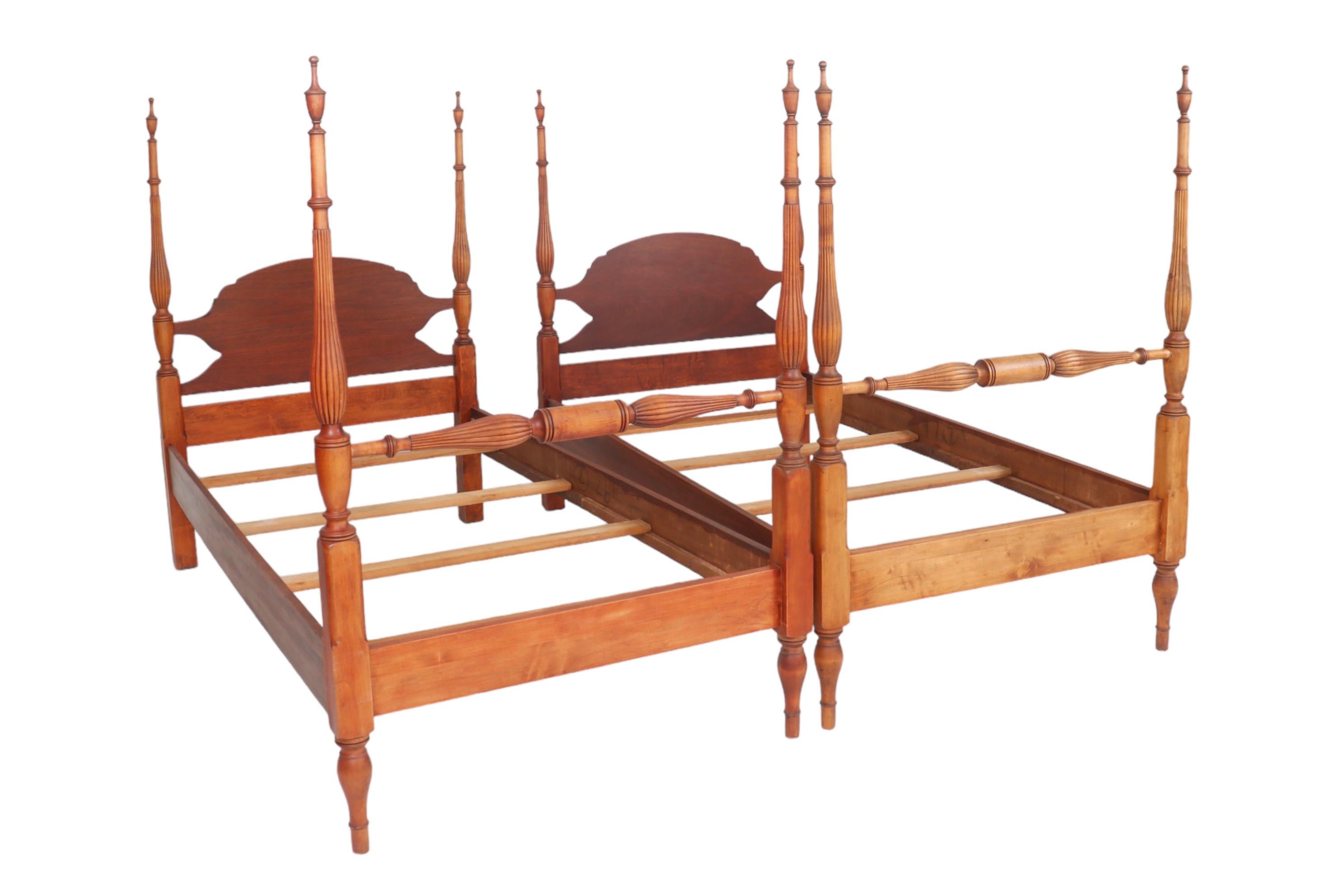 A pair of colonial style four poster twin beds made of mahogany. Each bed frame has four turned and reeded posts topped with urn finials and finished with turned arrow feet. Top posts are connected with carved oval headboards and the foot posts are