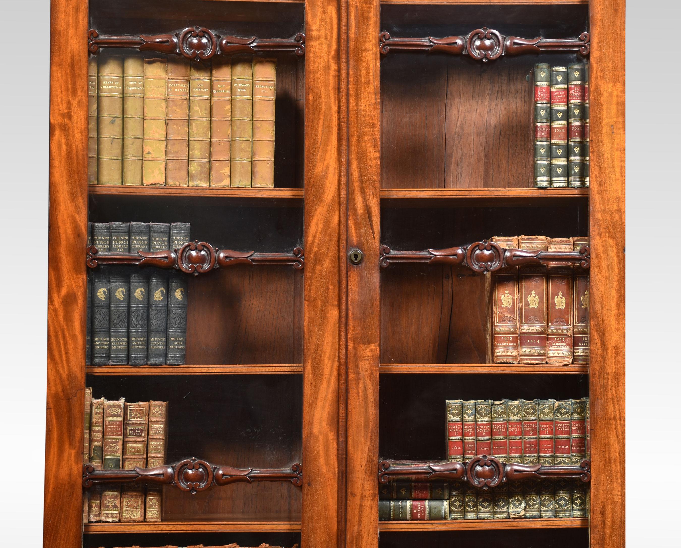 Mahogany bookcase of narrow proportions. The molded cornice above a pair of glazed doors with decorative scrolling glazing bars enclosing adjustable shelved interior. To the base fitted with a pair of panelled doors opening to reveal two long