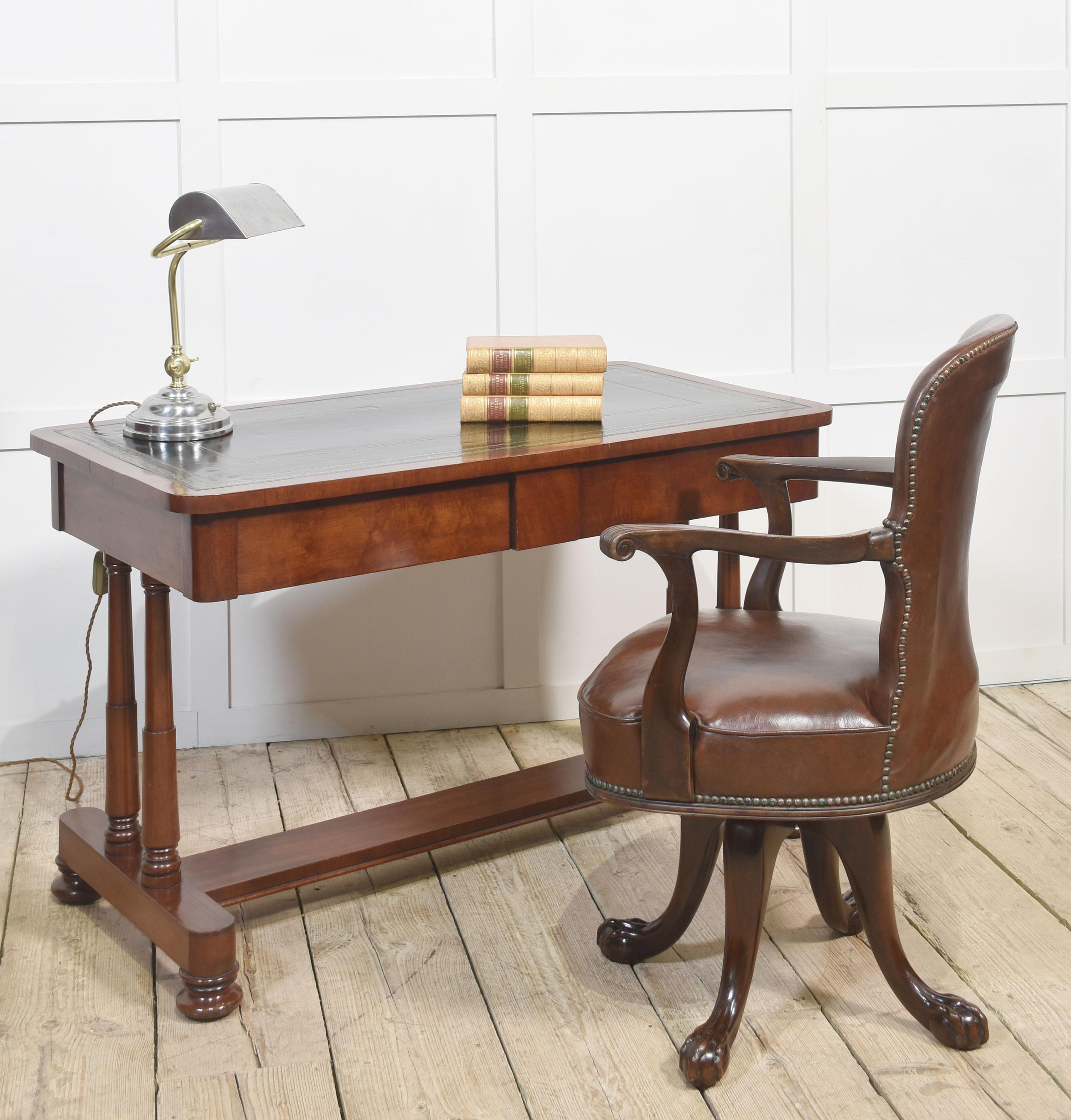 Mahogany writing table the large rectangular top with inset black tooled leather with gilt-tooled border. Above the frieze fitted with two drawers, all raised up on cylindrical supports united by stretchers, termanatting in bun feet with recessed