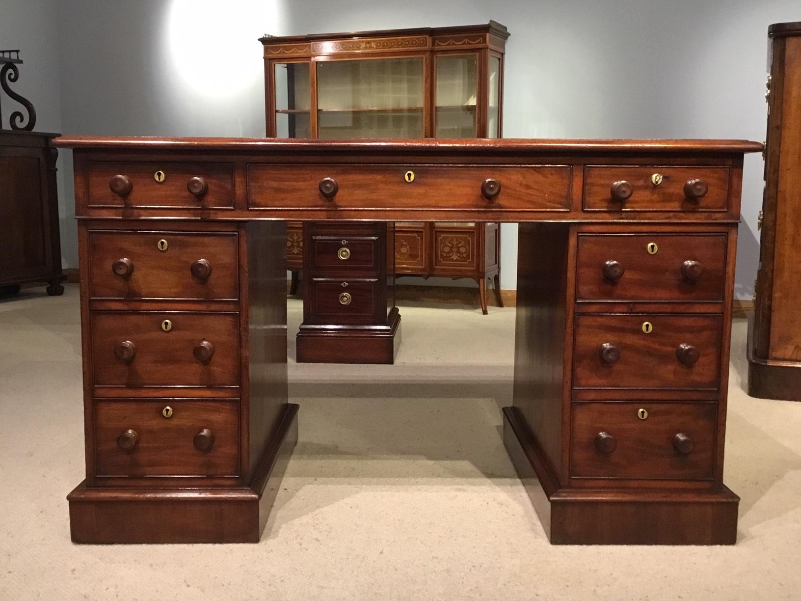 A fine quality mahogany Victorian period antique pedestal desk. Having a rectangular mahogany top with an inset red leather writing surface with gilt tooled detail and having an arrangement of nine rectangular mahogany lined drawers with turned