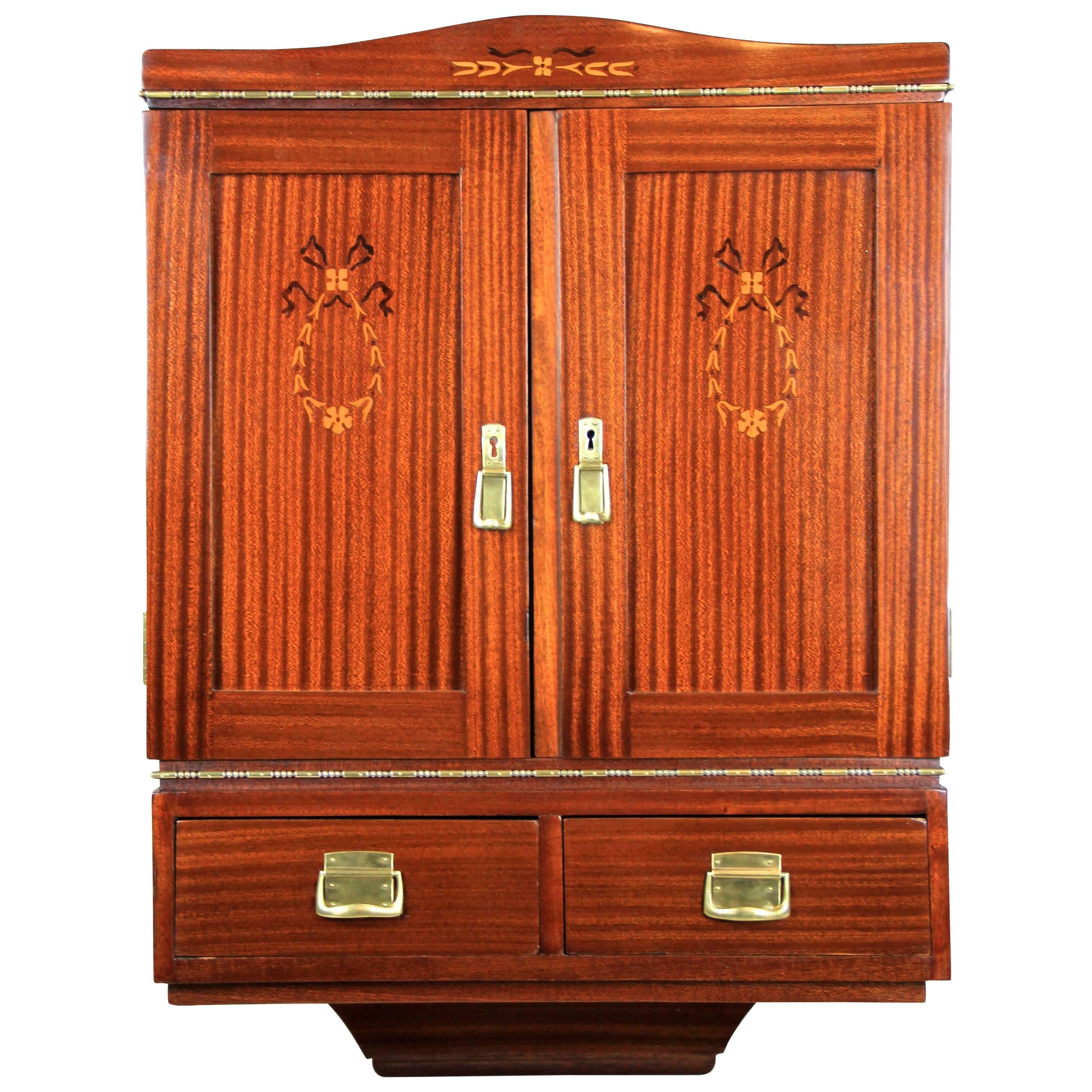 Appealing mahogany wall cabinet from the Art Nouveau period in Austria, circa 1910. Made with finest mahogany veneer, this small wall-mounted cabinet offers two doors with beautiful inlay works in walnut and maple and two small drawers all veneered