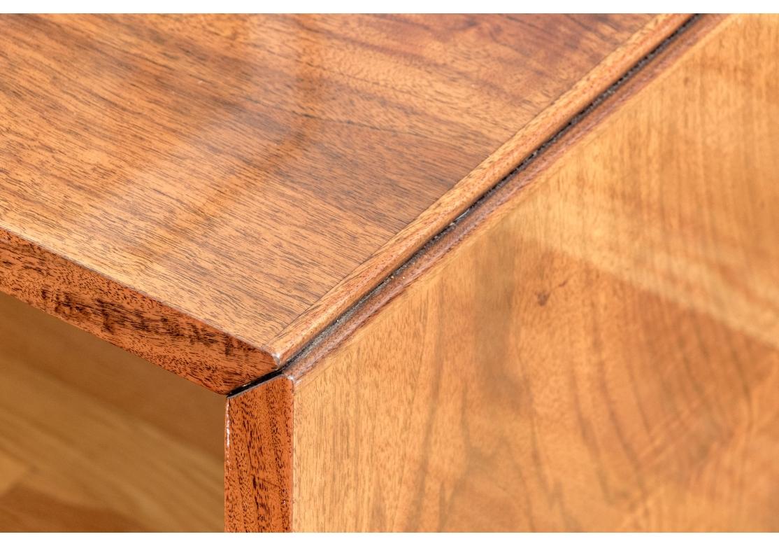 Una elegante mesa de cóctel con un elegante perfil de cascada en caoba marrón cálido artísticamente combinada. La sencilla construcción a inglete de la mesa le confiere una elegancia atemporal con una funcionalidad brutalista equilibrada por el