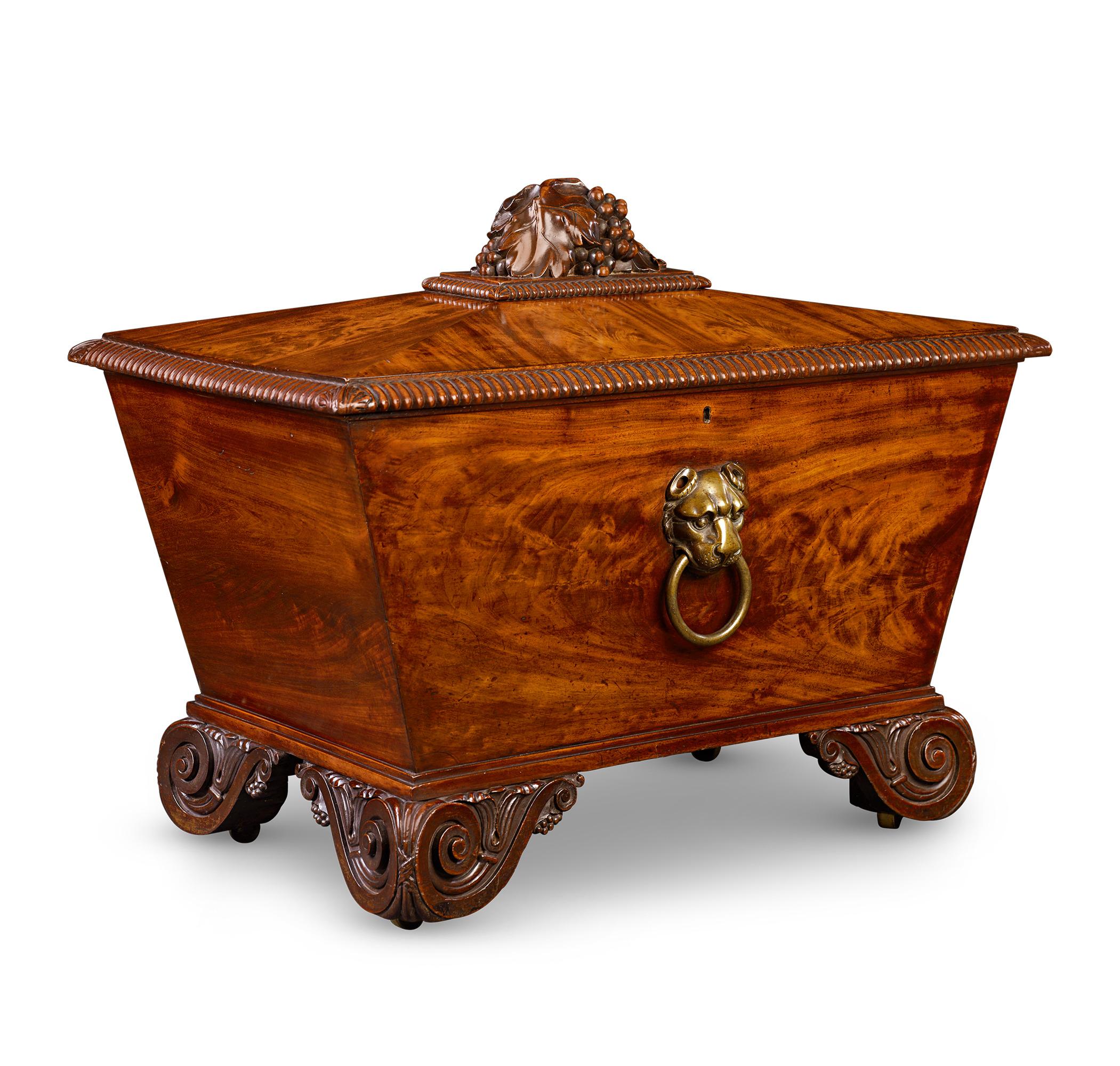 This exquisite 19th-century wine cooler is sculpted from the finest mahogany into a distinctive sarcophagus shape. The top is adorned with intricately carved grape and grape leaf motifs, framed by gadrooned borders. The piece rests on elegantly