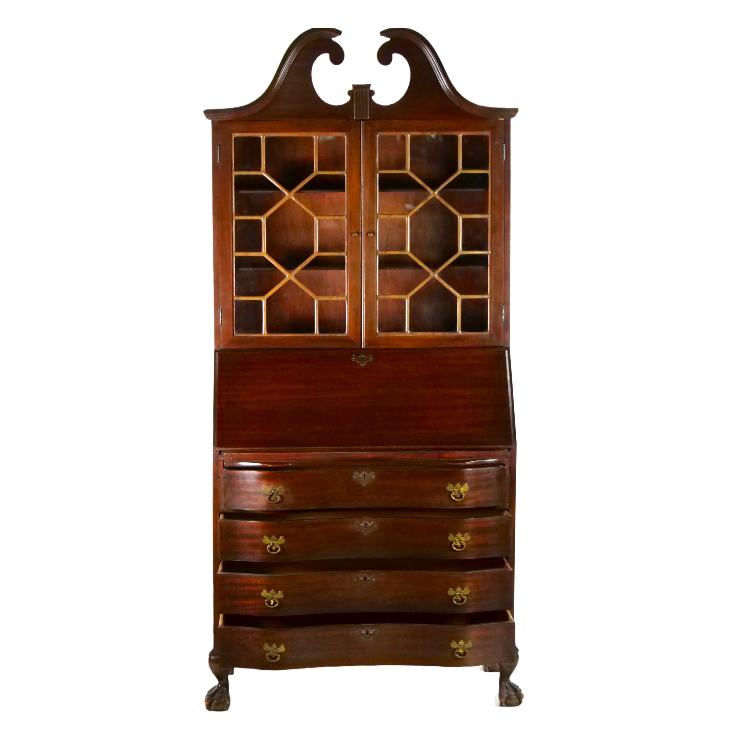 Chippendale style mahogany wood secretary desk / bookcase cabinet with slant front detail in one piece construction. The Upper cabinet features two wood framed glass door panels and two adjustable wood shelves behind dual glass doors with fretwork.