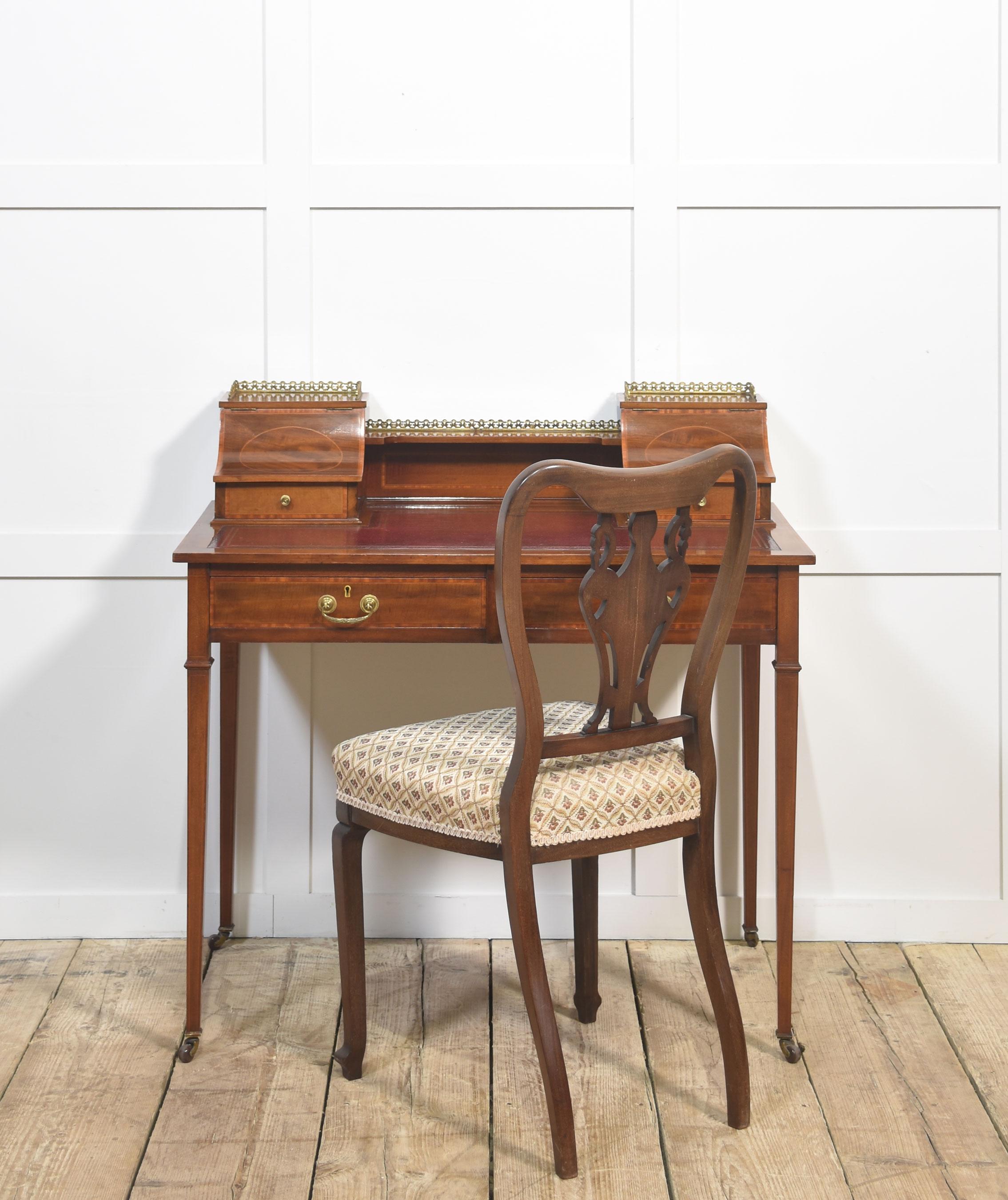 A fine quality Edwardian mahogany writing desk featuring elegant satinwood inlay and a rich patina. The desk is fitted with a tooled red leather writing surface, complemented by a pair of curved-front stationery boxes with small drawers and brass