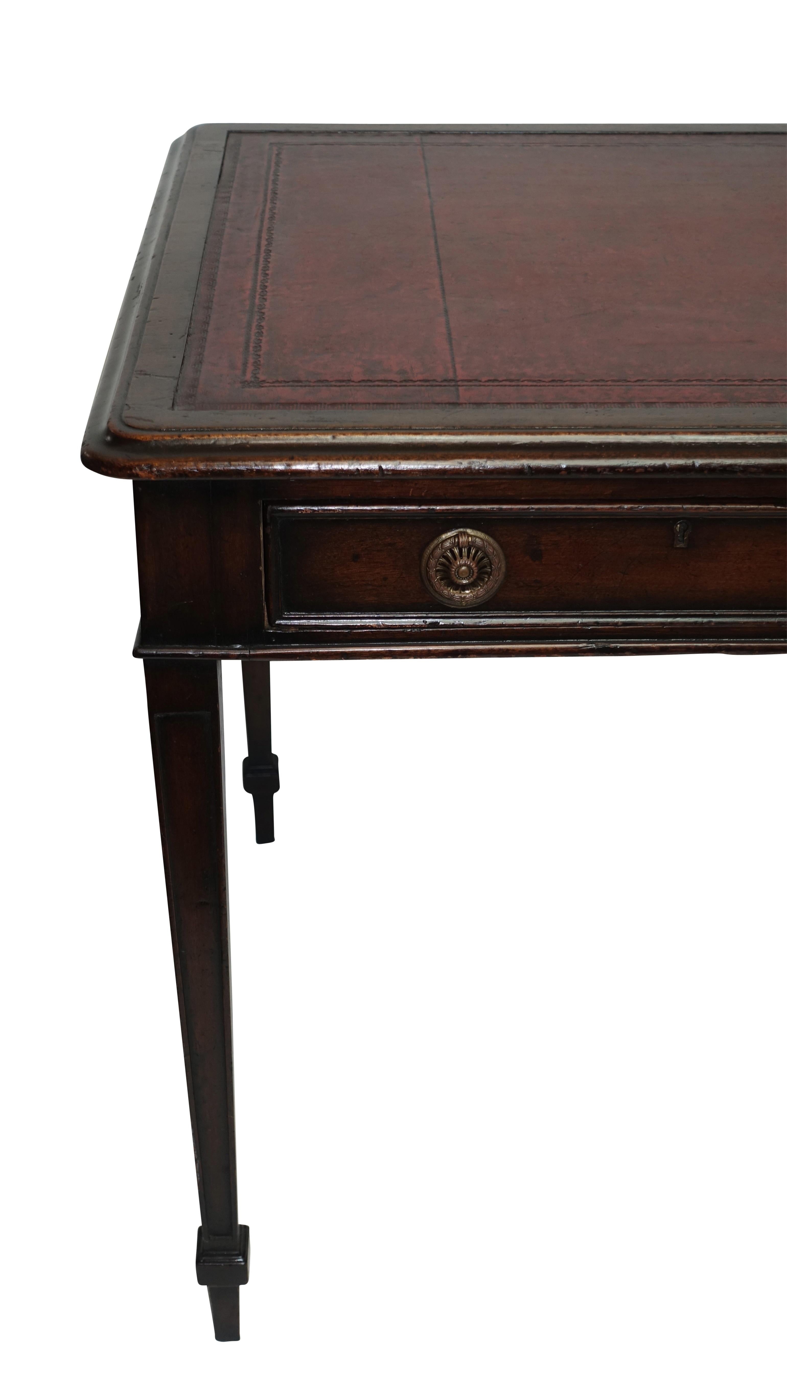 Mahogany writing table desk with inset embossed red leather top above two drawers standing on square tapering legs with cuffed foot. England, early to mid-19th century.