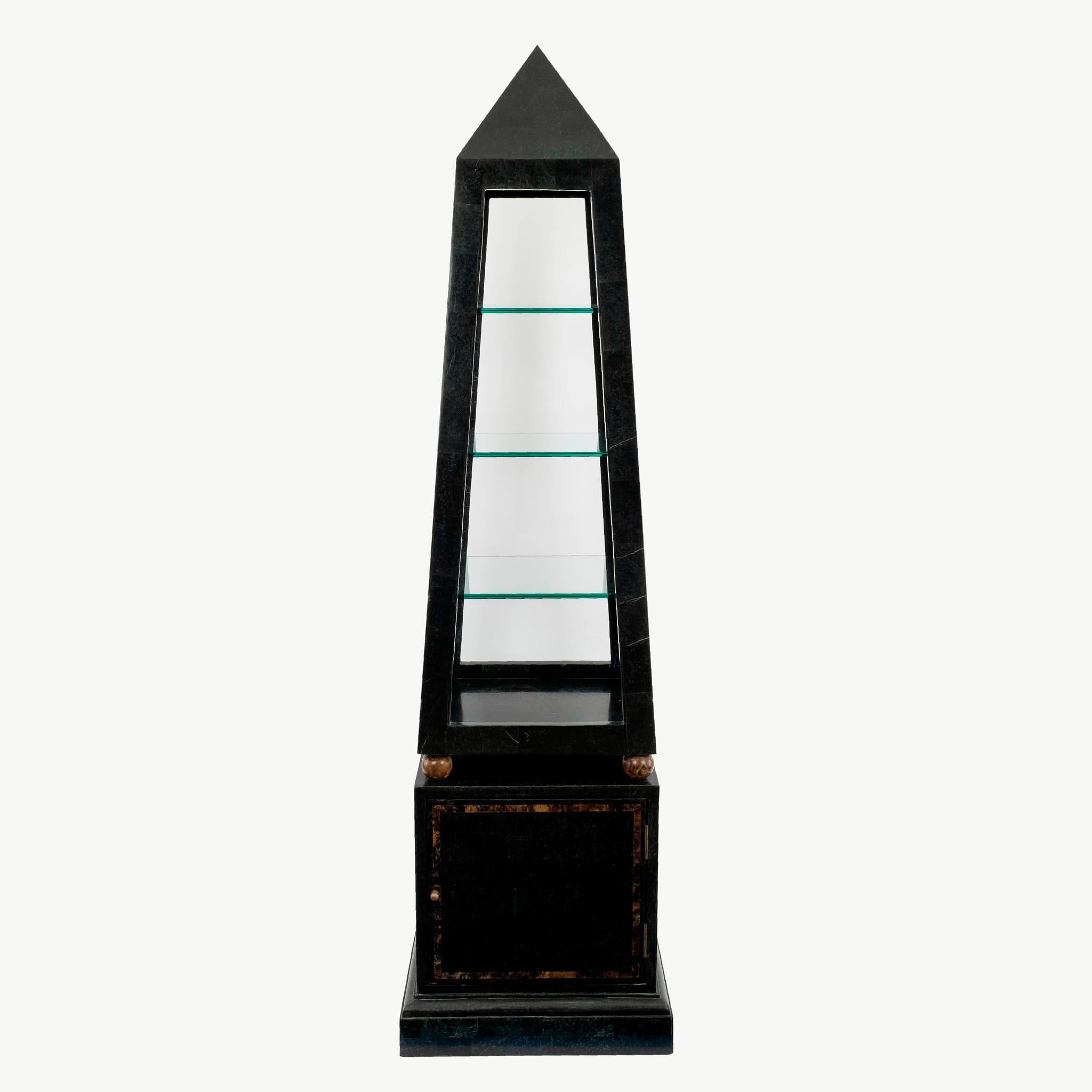 Vintage tessellated black marble and brass obelisk shaped etagere with three glass shelves and one cabinet door for storage.