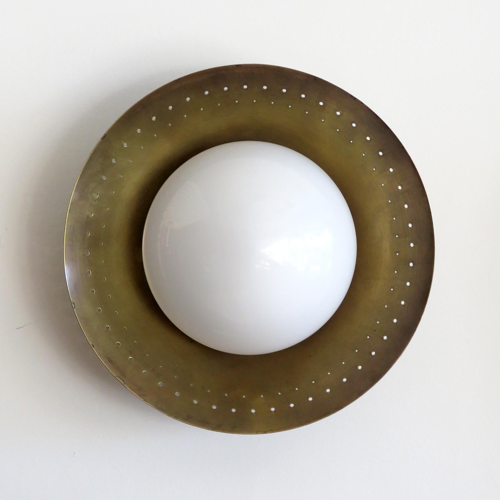 Elegante Wandleuchte Maine, entworfen von Gallery L7, handgefertigt und fertiggestellt in Los Angeles aus amerikanischem Messing, mit mittigem Opalglasschirm auf einer gealterten, rohen Messingscheibe mit wunderschönen Randperforationen. Eine
