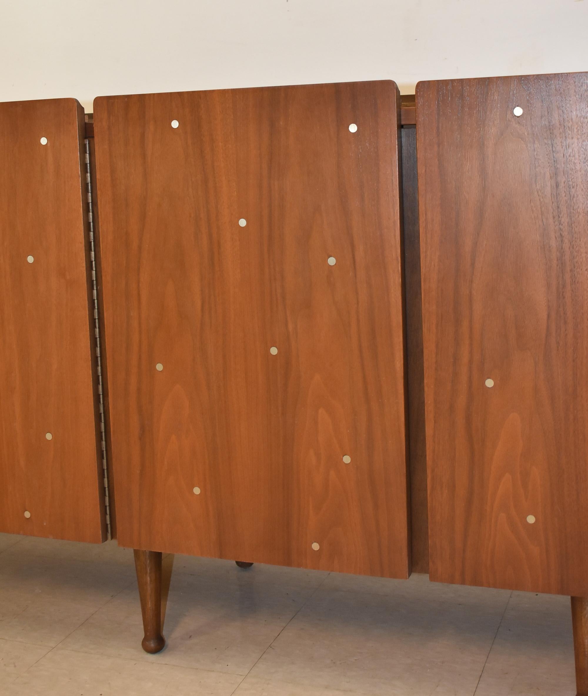 4-door walnut credenza or low dresser from Mainline by Hooker Furniture. Doors are accented with inlaid brass discs and cover fitted interiors with drawers. The piece sits on 6 turned legs with ball feet, and is believed to be custom made. Excellent
