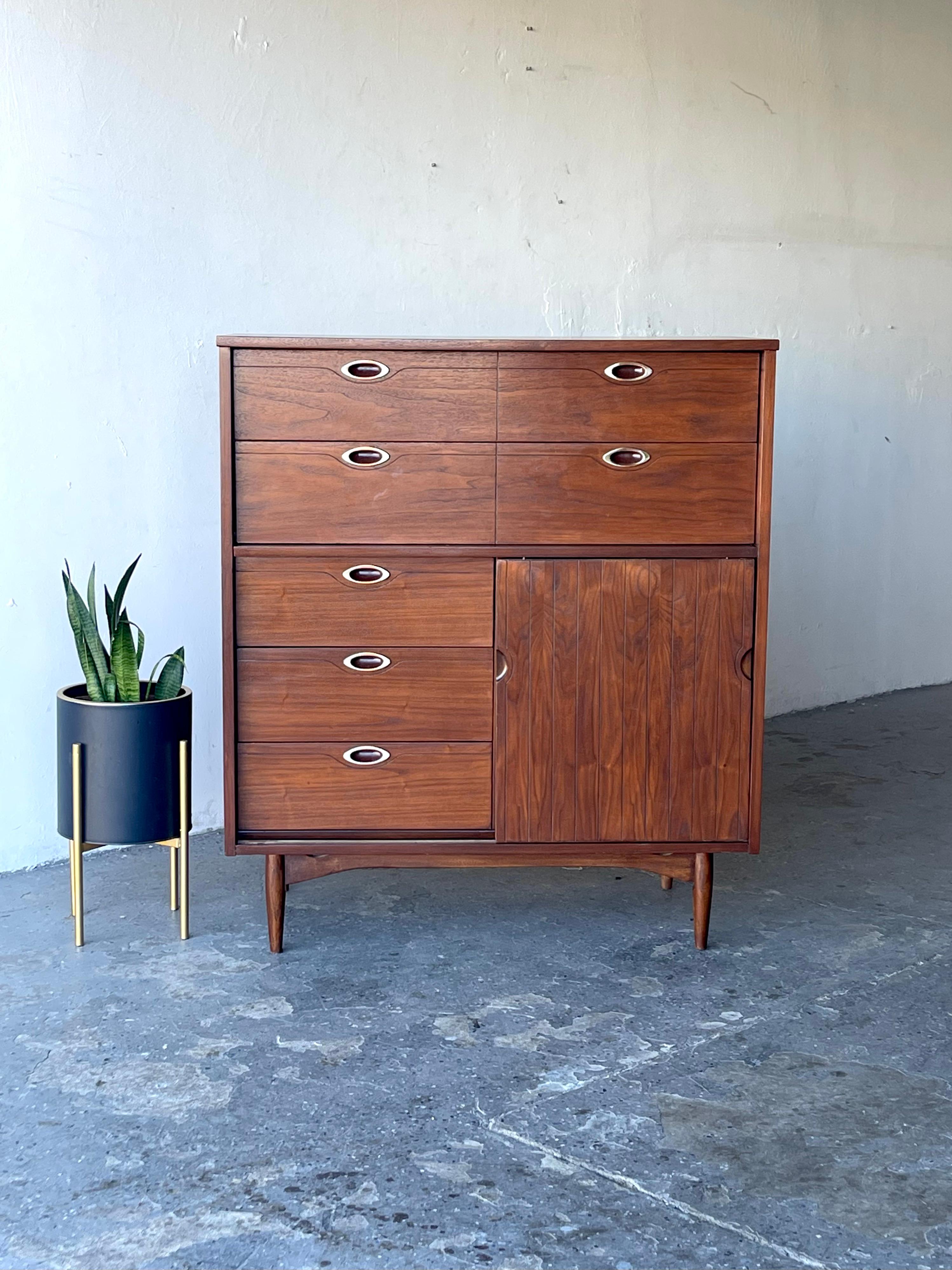 This exceptional Mid Century Modern Gentleman’s Chest from the Mainline collection by Hooker Furniture Company features a total of eight drawers, three of which are hidden behind a sliding panel.  This piece provides maximum storage capacity with