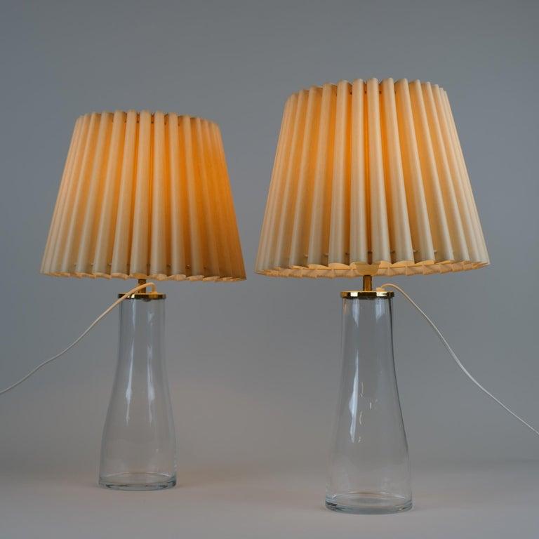 Un par de lámparas de mesa modelo M15 de latón y cristal transparente con pantallas de color amarillo cálido, diseñadas por Maire Gullichsen para Artek en la década de 1960. Este diseño sencillo pero elegante es uno de los pocos artículos diseñados