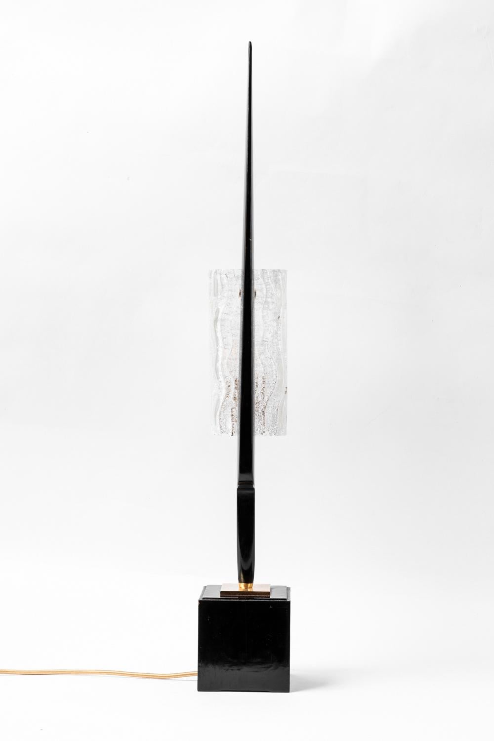 Maison Arlus, attributed.
Lamp in black lacquered wood and glass. Cubic base in black lacquered wood supporting a black slim form in which a rectangular thick lampshade in glass, carved with waves patterns, is inscribed in.

Work realized in the