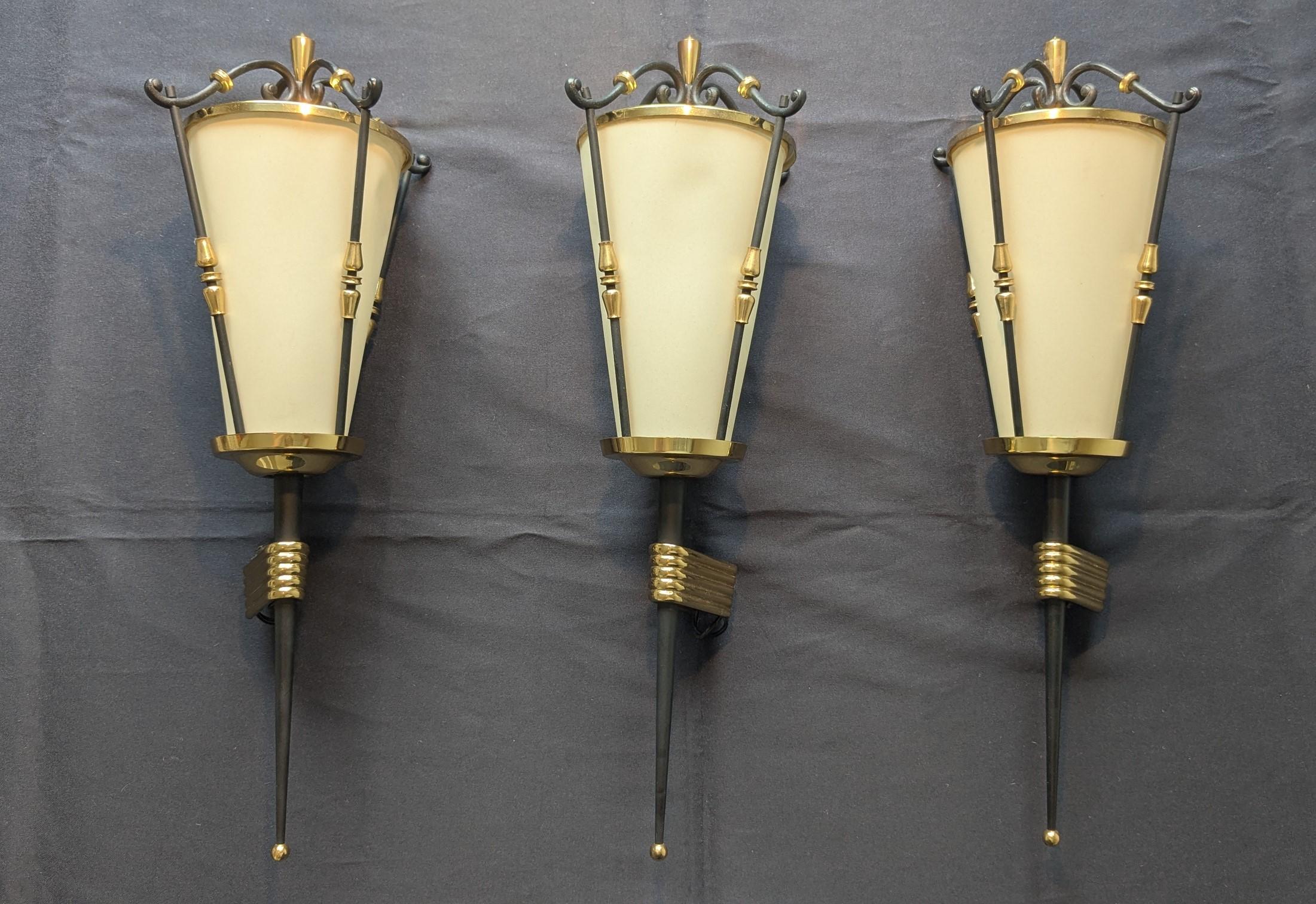 Elegantísimo conjunto de 3 apliques altos estilo linterna de Maison Arlus, fabricados en Francia en los años 50 Mid Century Modern en latón dorado y hierro forjado ennegrecido con detalles muy bonitos, que crean un precioso contraste entre las
