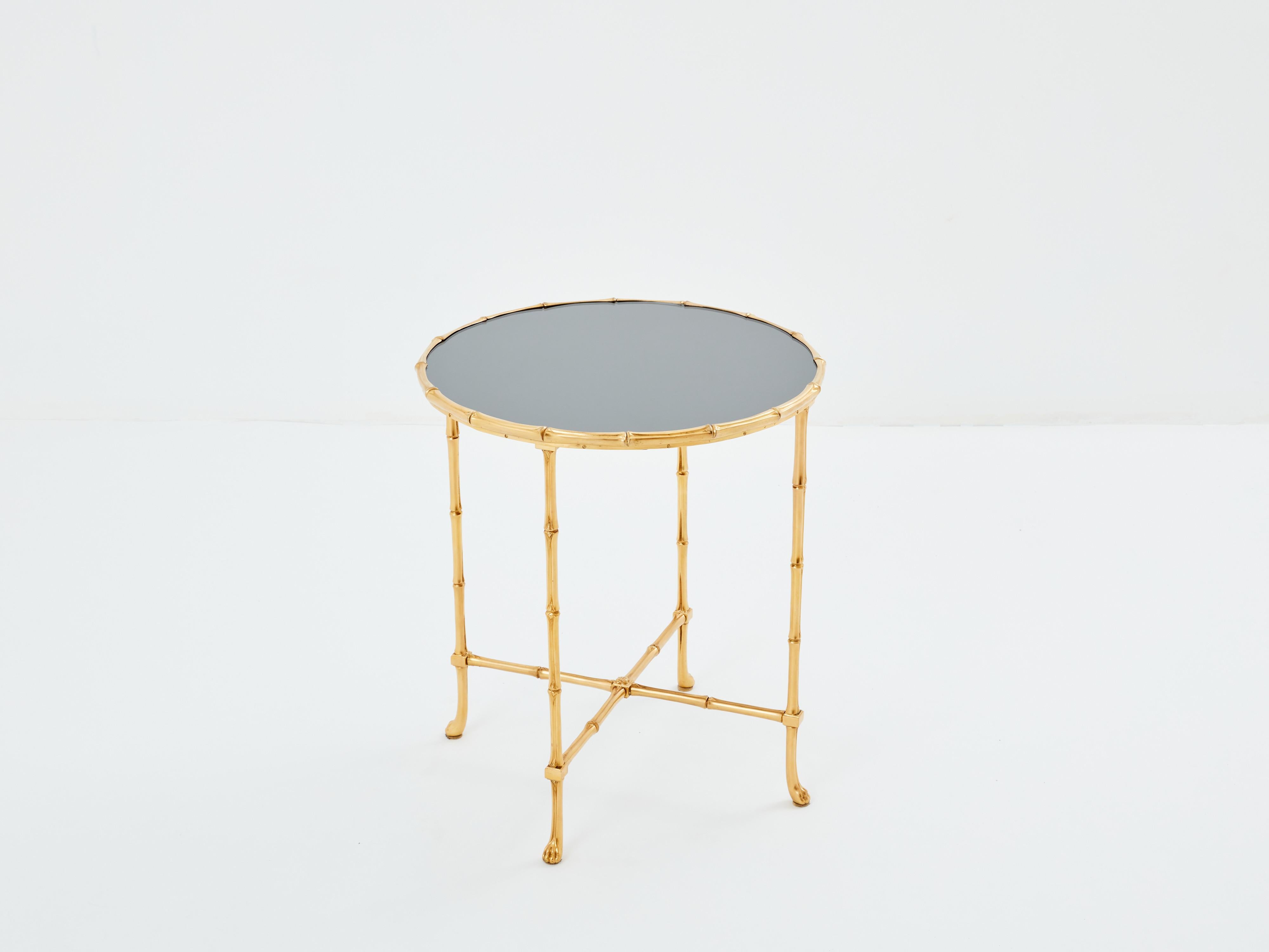 This beautiful Maison Baguès gueridon table was created with solid bamboo shaped brass and a beautiful dark grey mirror top in the early 1960s. The dark grey mirror top is timeless and smooth, while the brass bamboo feet and body provide an