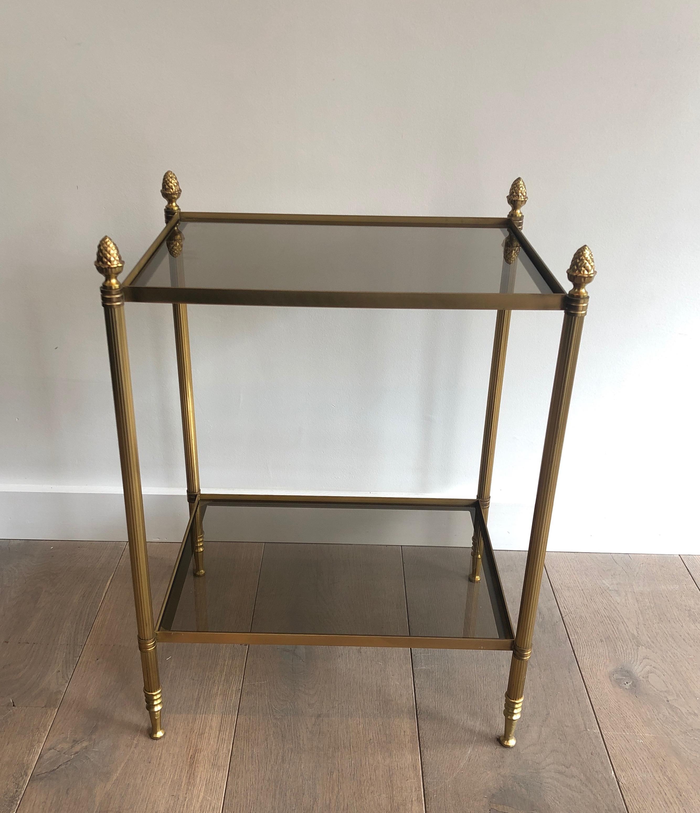 This neoclassical style side table is made of brass with smoked glass shelves. This is a very nice and fine work with fluted legs and nice chiseled finials on each corner. This work is by famous French designer Maison Baguès, circa 1940.