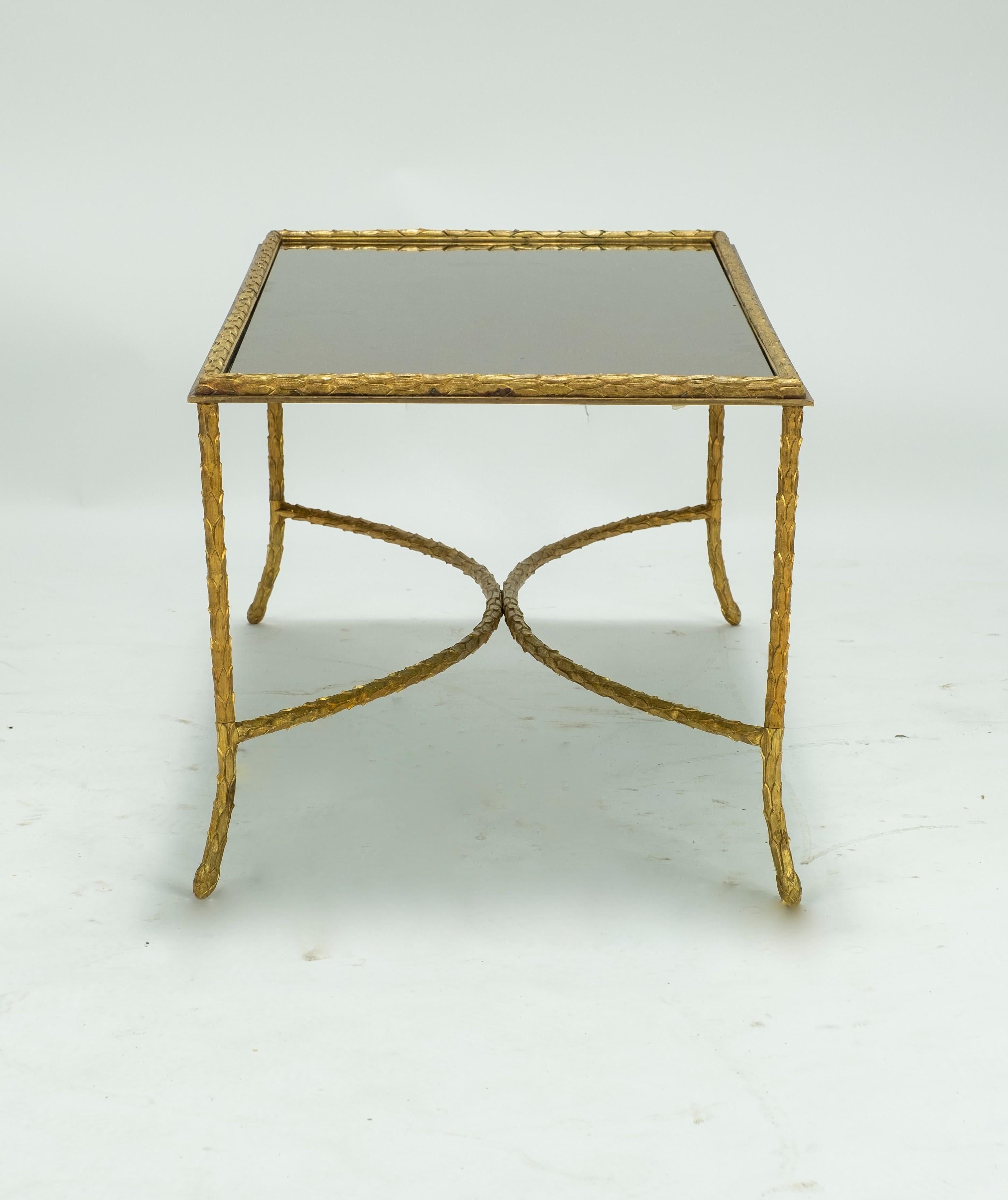 A substantial Baguès bronze coffee table having foliate theme and smoke mirrored top circa 1940. Gilt leaves are on the perimeter of mirrored glass and throughout the 4 legs and base of the cocktail table.