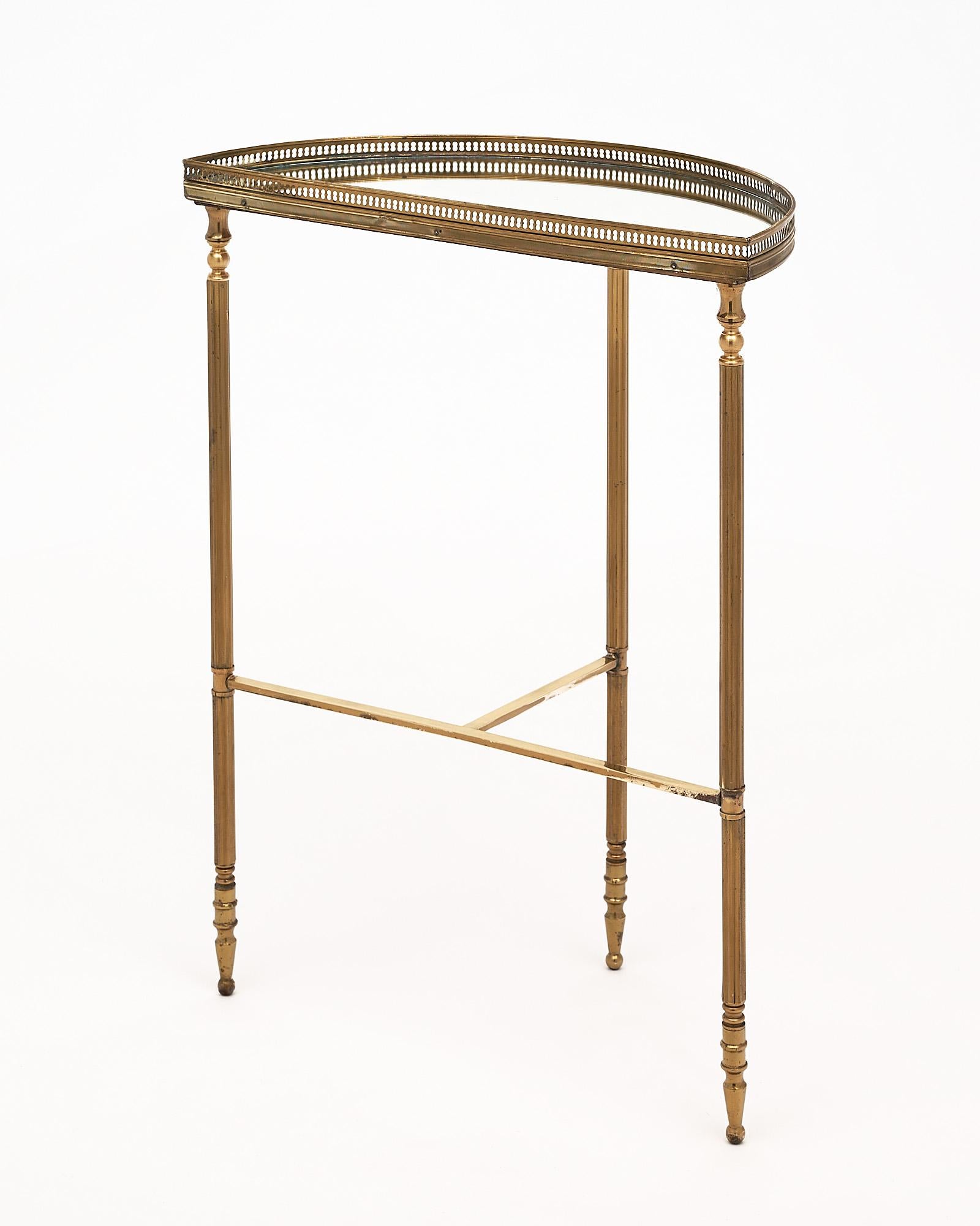 Demilune console, French, by Maison Bagues. There is a mirrored top with an opened brass gallery and ridged brass legs held together with a stretcher.