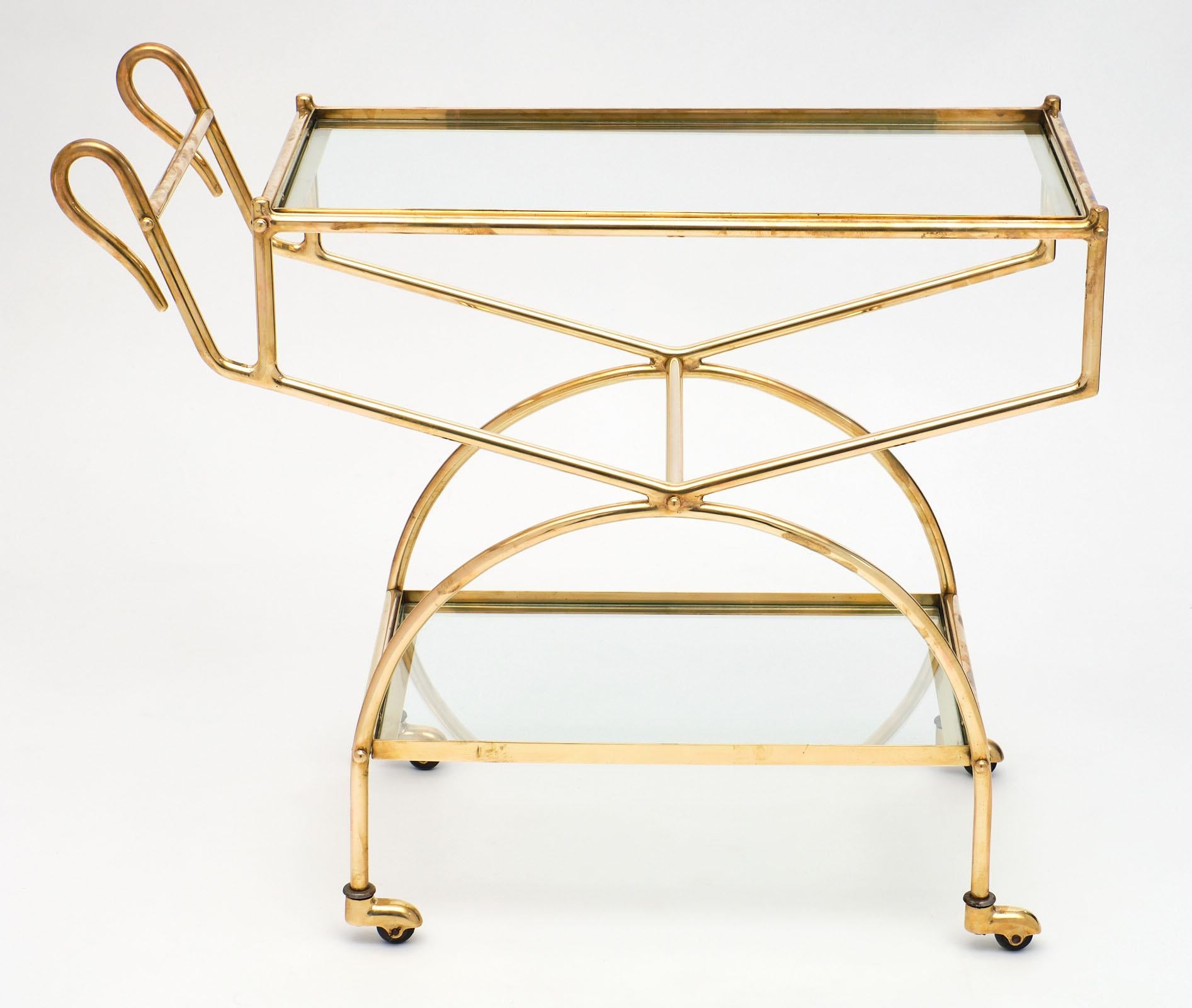 French Maison Baguès brass bar cart with two levels of clear glass. The gilded brass is in impeccable condition with beautiful curved stylized swan-neck handles.
