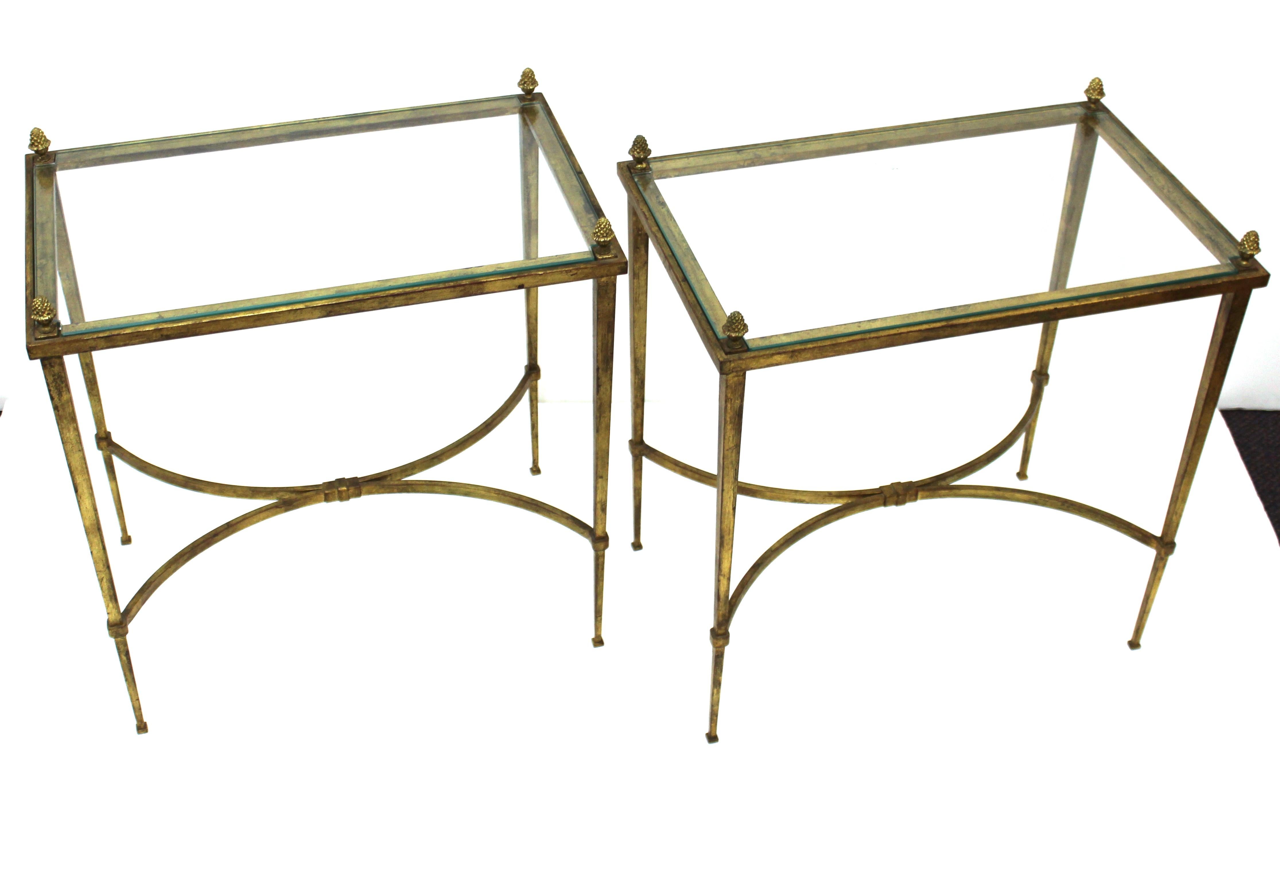 Hollywood Regency pair of end tables or side tables made by Maison Baguès in France during the mid-20th century. The pair is made of gilt bronze in a neoclassical inspired style and has rectangular glass tops and finials. In great vintage condition