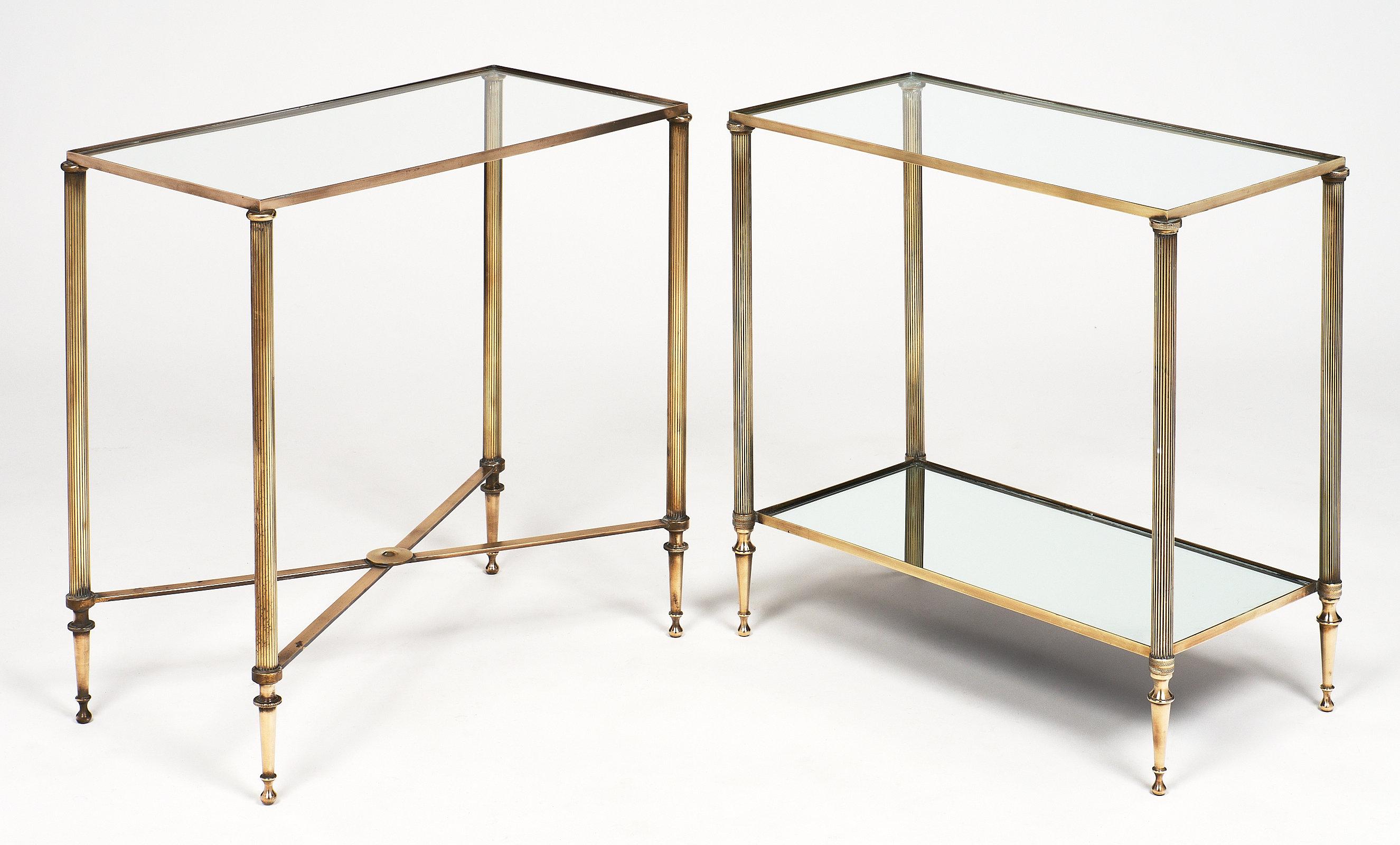 Fine French set of side tables by Maison Baguès. These brass tables each feature a glass top and tapered legs. They are a faux pair, as one has a mirrored lower shelf, and the other has an X-shaped stretcher. The tables differ in size only slightly.