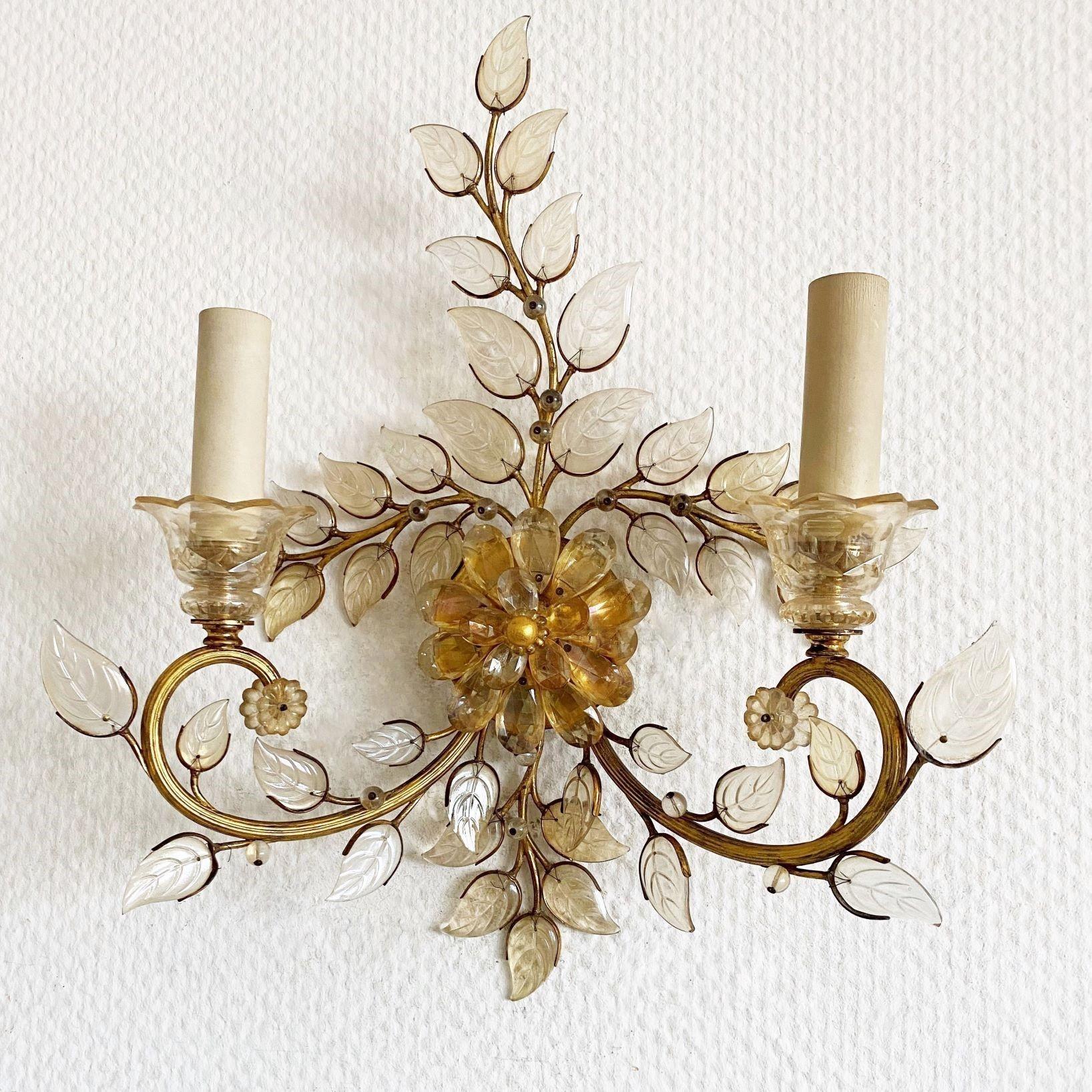 An elegant Maison Baguès gilt-brass two-branch wall sconce, France 1950s. Beautifuly decorate with glass leaves and a central flower with amber crystal elements, two cut crystal tulips holding the candle sleeve-lights, brass round back base. The