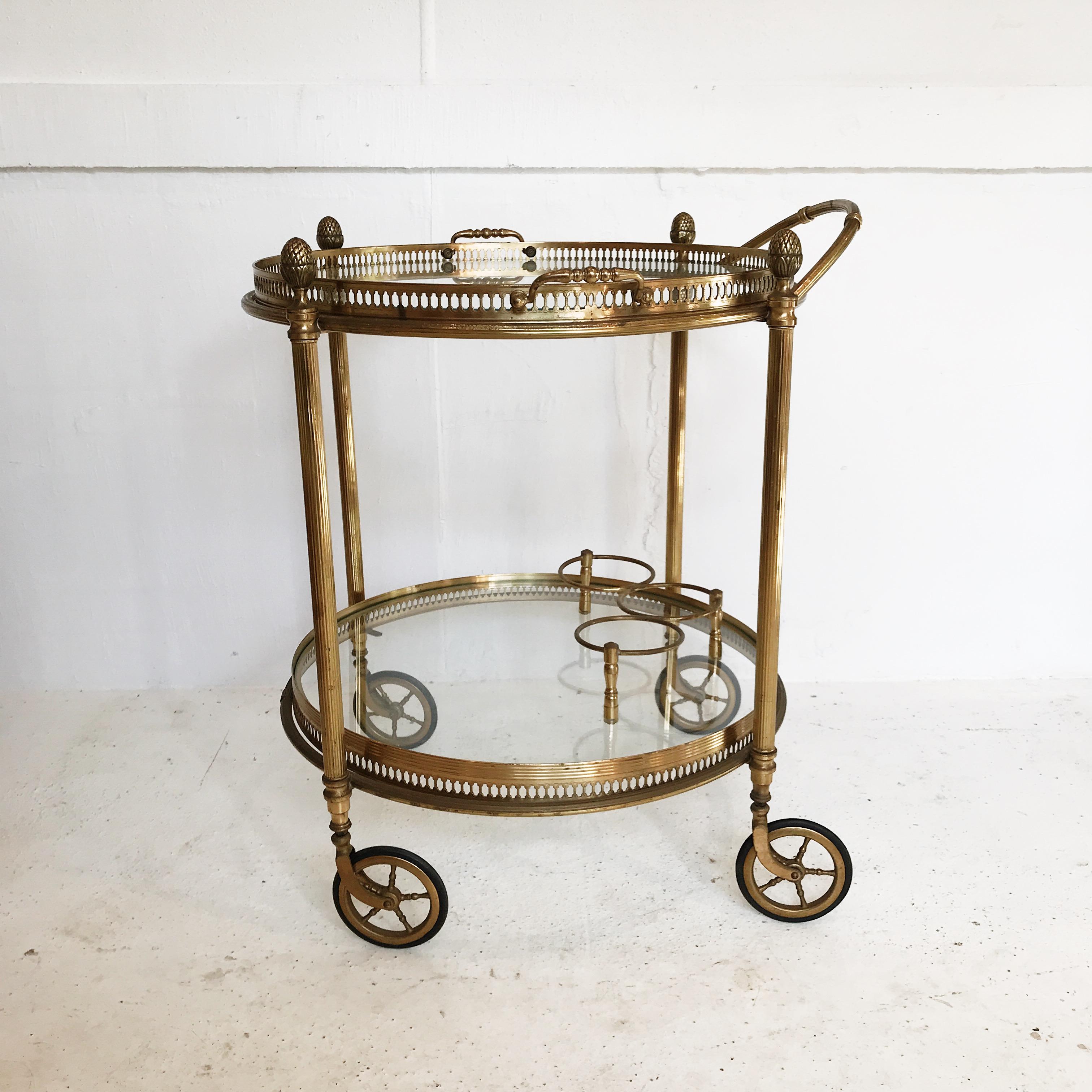 An enchanting 1940s vintage, Maison  Baguès, two-tier drinks cart/serving trolley in gilt brass. Features two round glass tiers, each with pierced galleries, and is adorned with acorn finials. Bottom tier includes attached 