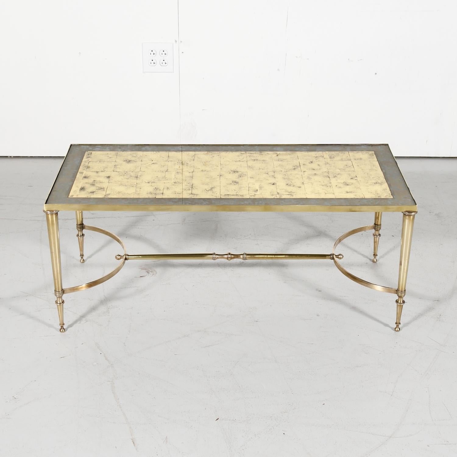 Stunning midcentury French brass and glass cocktail or coffee table by renowned French design house Maison Baguès features an inset mirrored glass top with a beautiful cloud like verre églomisé or gold mirroring, circa 1950s. The tapered legs are