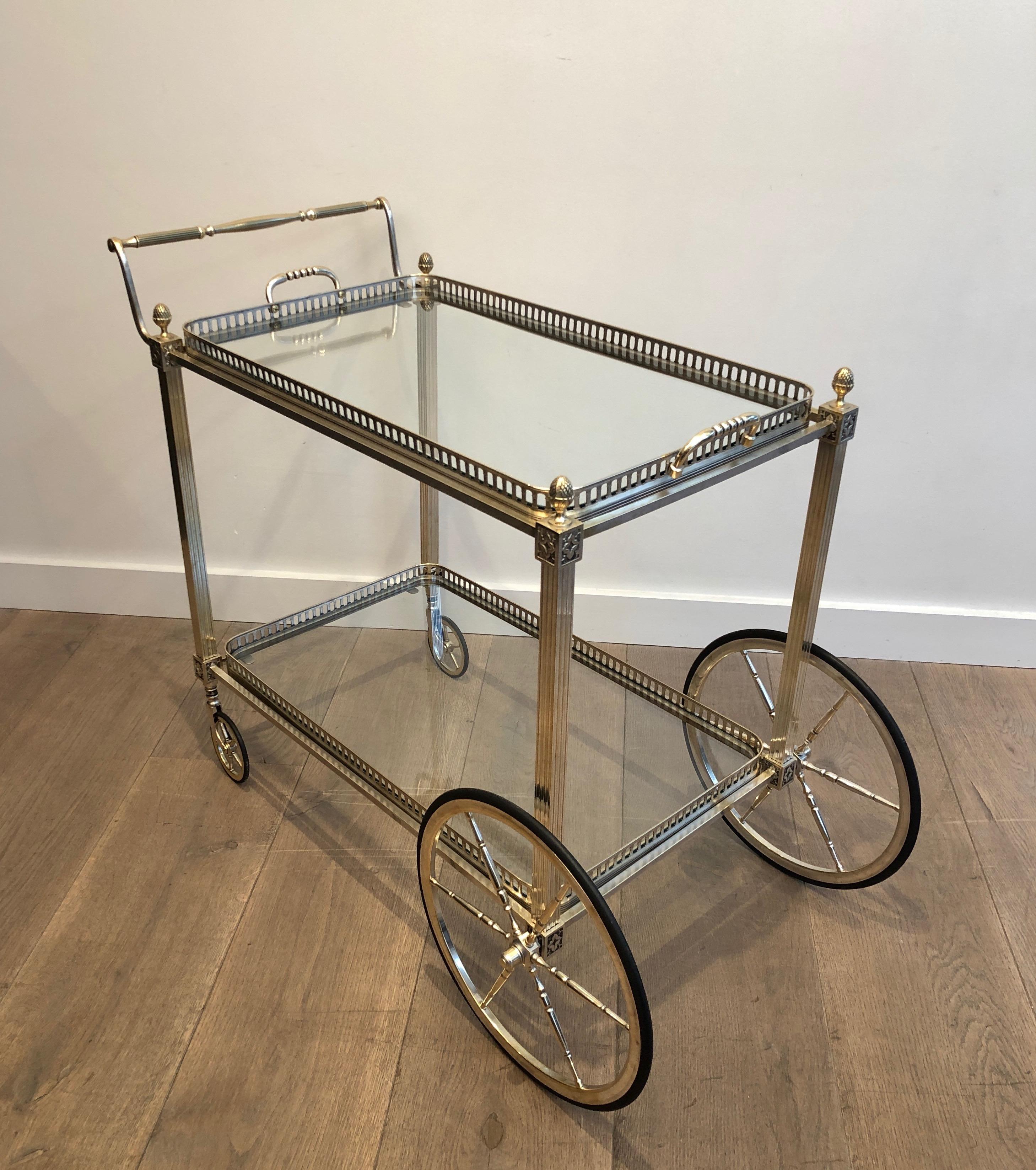 This neoclassical style bar cart is made of silver on brass with Decorated with fleurs de lys decor. The silver is a bit used by time which makes a very nice silver and brass patina. This is a French work by famous French designer Maison Bagués,