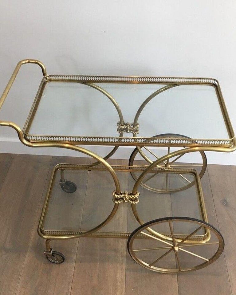 This neoclassical style bar cart is made of brass with glass shelves. It has nice bronze noodles on each side. This is a French work, circa 1940.