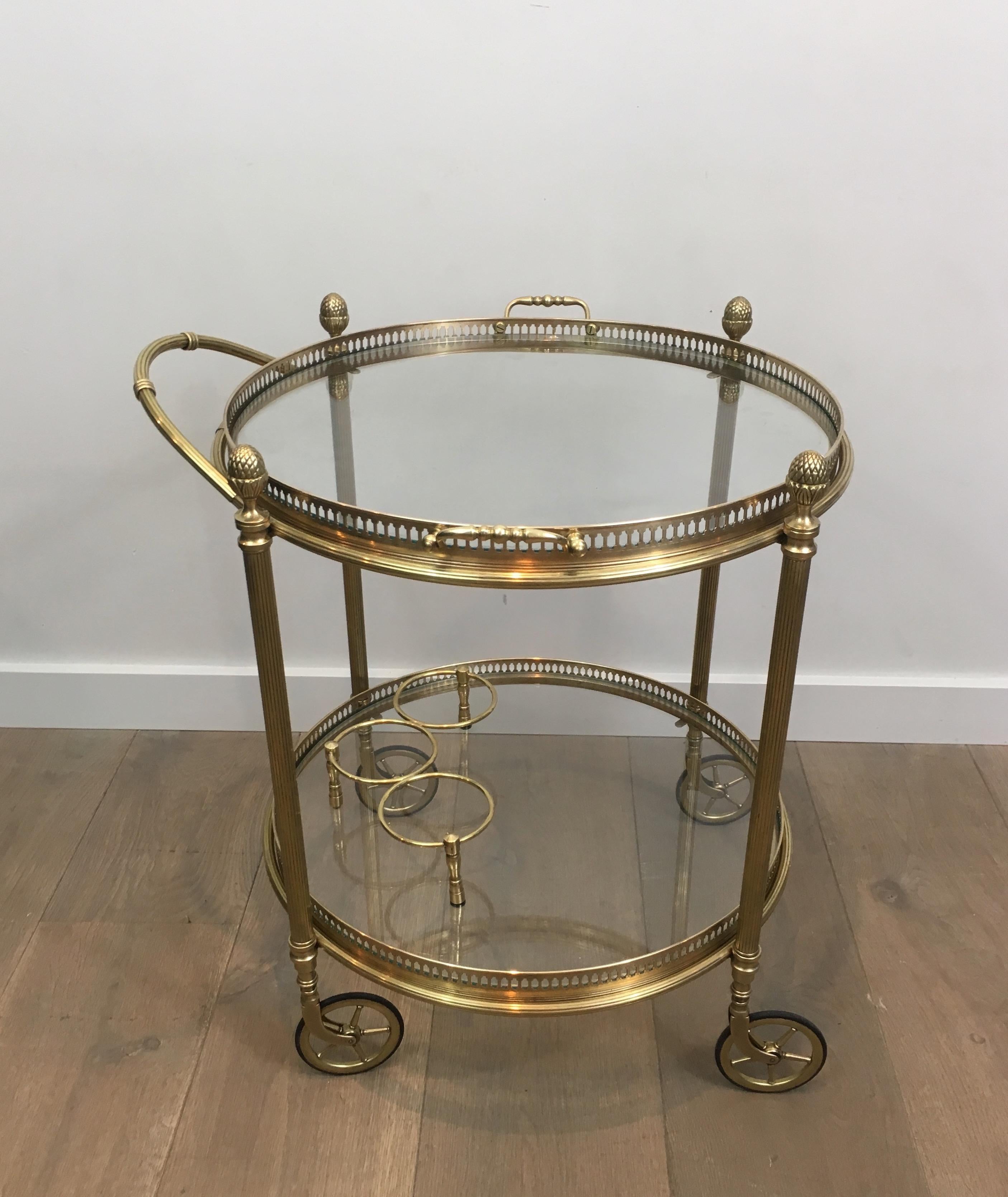 This very nice neoclassical round bar cart is made of brass and glass. This drinks trolley has 2 removable glass trays surrounded by a fine brass gallery with handles on top tray and with bottles holder on bottom tray. This is a very nice work by