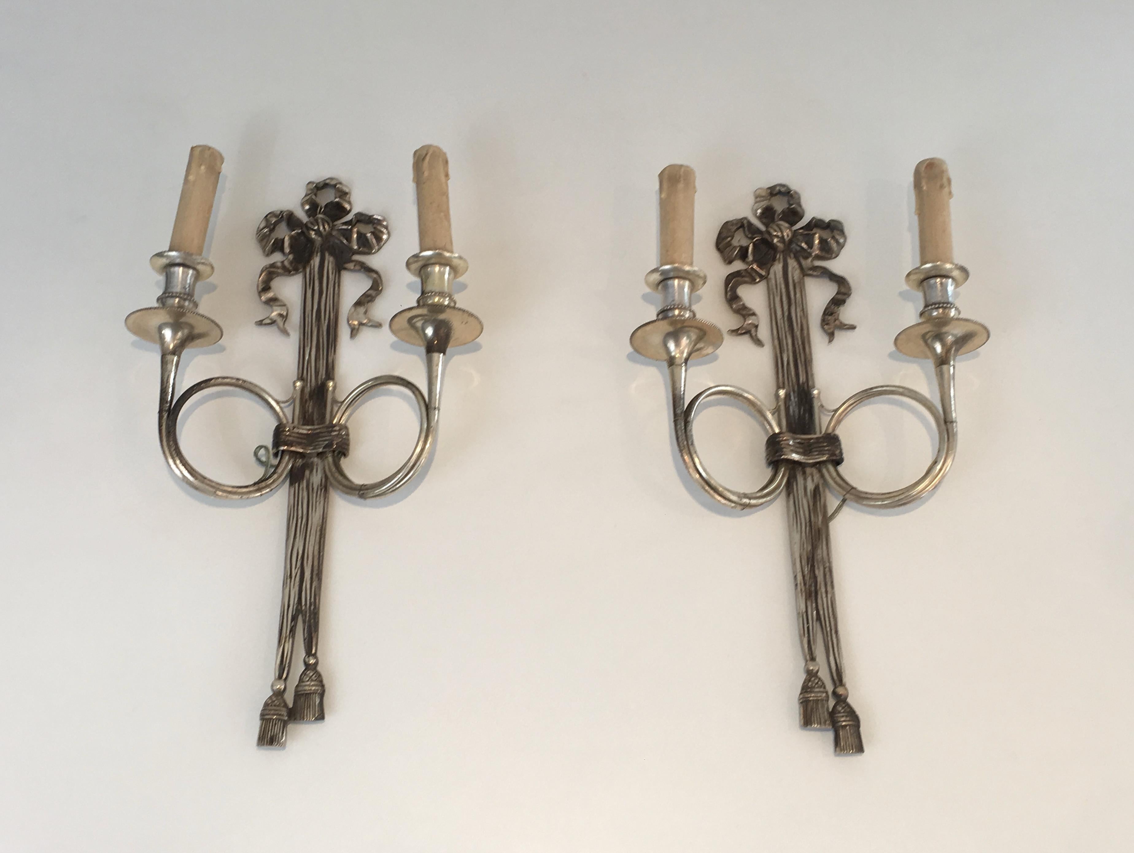 This very nice pair of neoclassical style wall sconces is made of silvered bronze. These wall lights are very decorative with their ribbon and hunting horns. These sconces were made by famous French designer Maison Baguès, circa 1960.