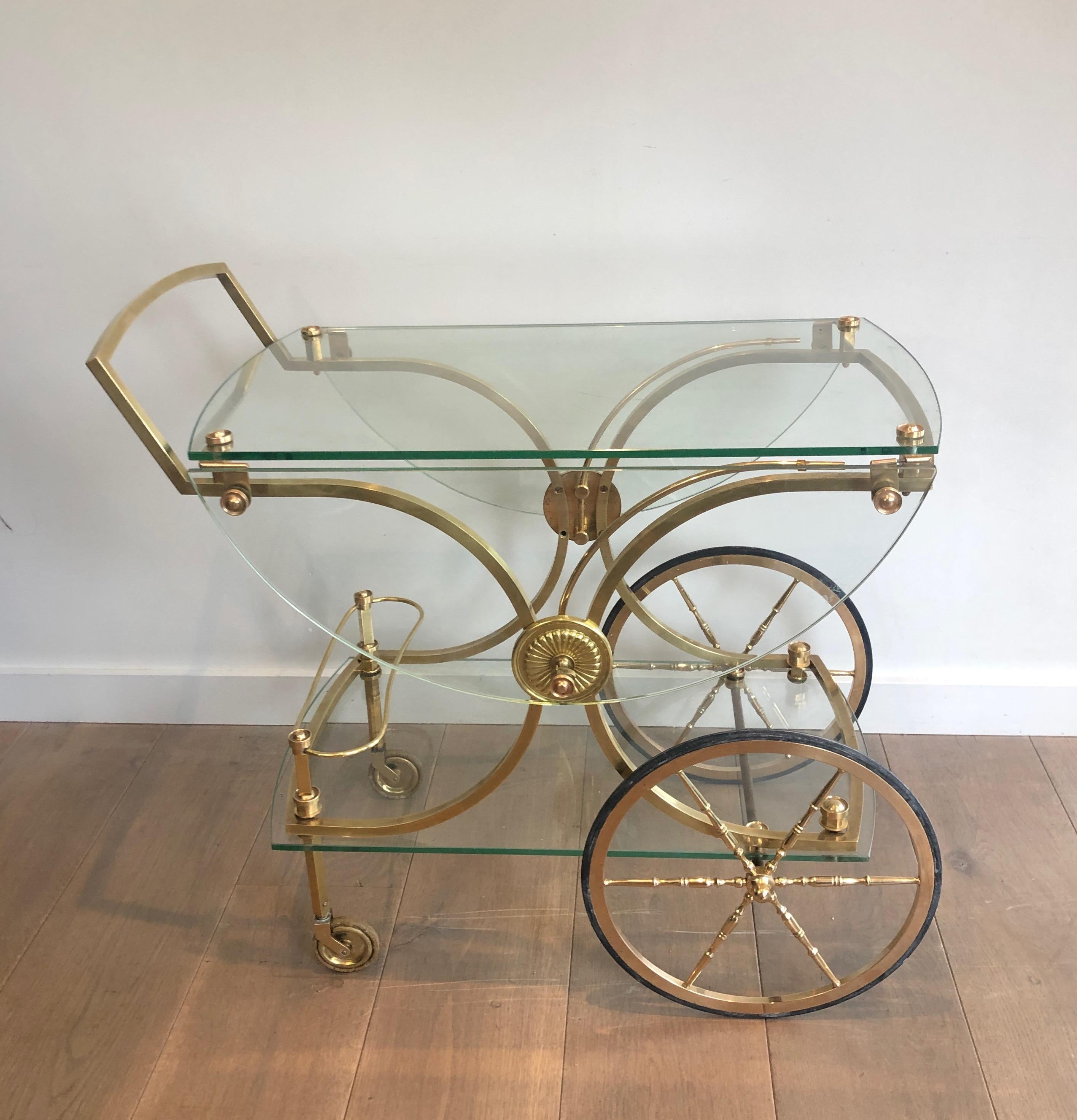 This rare neoclassical style bar cart is made of brass with glass shelves and removable rounded glass on the sides that can allow the drinks trolley to become a real round table. This is a work by famous French designer Maison Bagués, circa 1940.