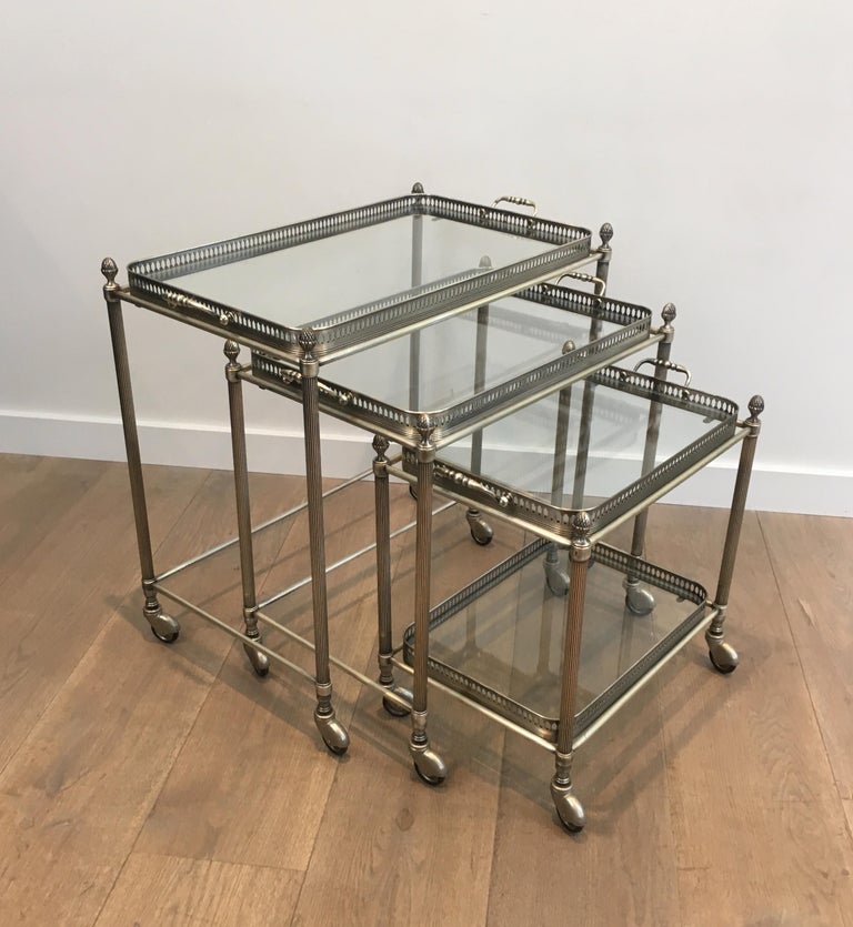 This rare set of 3 neoclassical style nesting tables on casters is made of silvered brass. These stacking tables were made by famous French designer Maison Bagués, circa 1970.