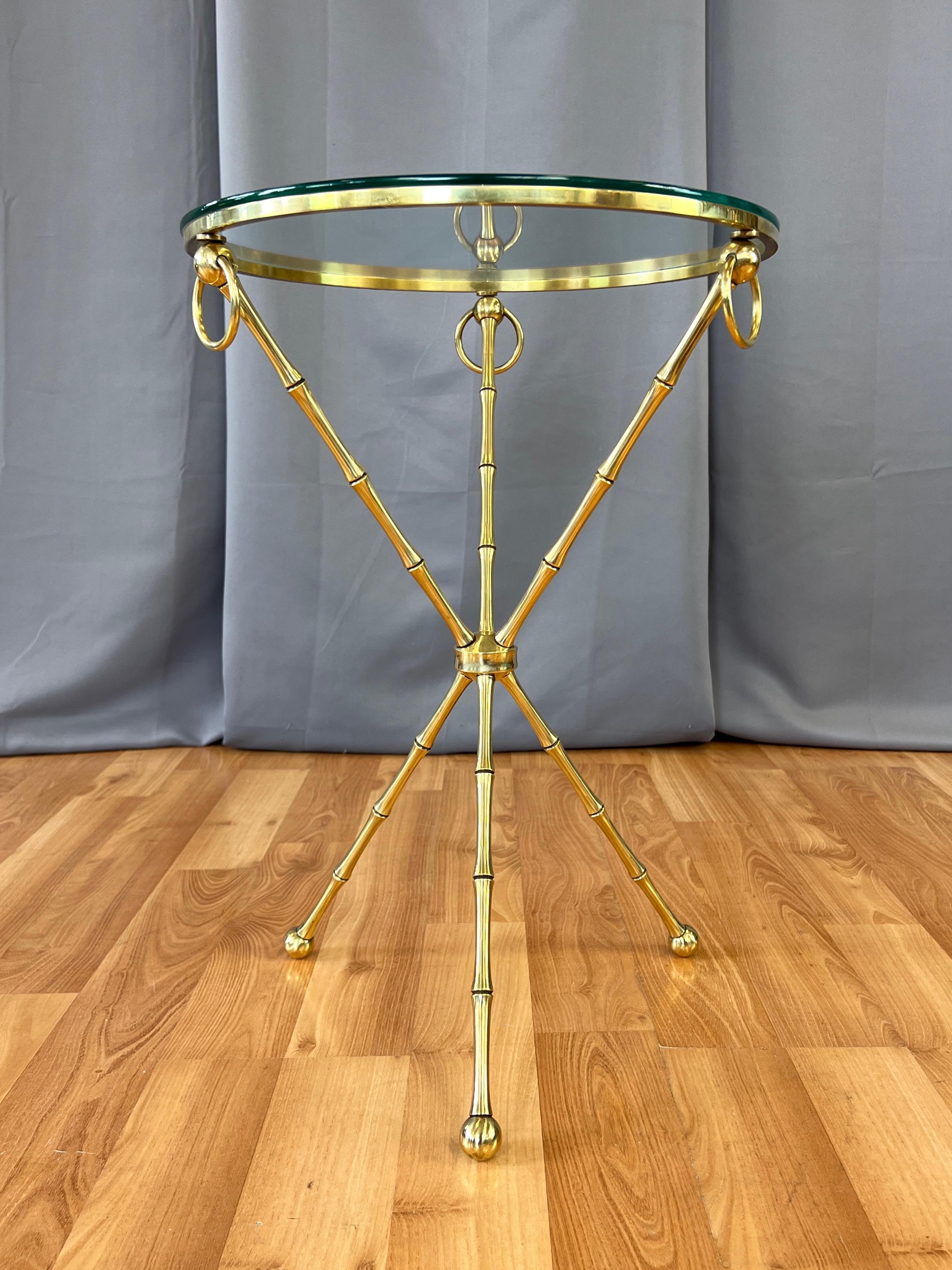 An elegant circa 1960 Hollywood Regency Maison Baguès or Maison Jansen-style brass faux bamboo tri-leg side table, occasional table, or guéridon with round glass top.

Gleaming solid brass frame with three intersecting faux bamboo legs on ball feet